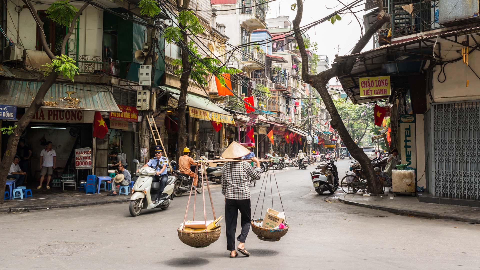 Hanoi, Vietnam - May 19, 2016: Street vendor carrying transporting goods in baskets using a carrying pole, also called a shoulder pole, in Hanoi's Old Quarter.