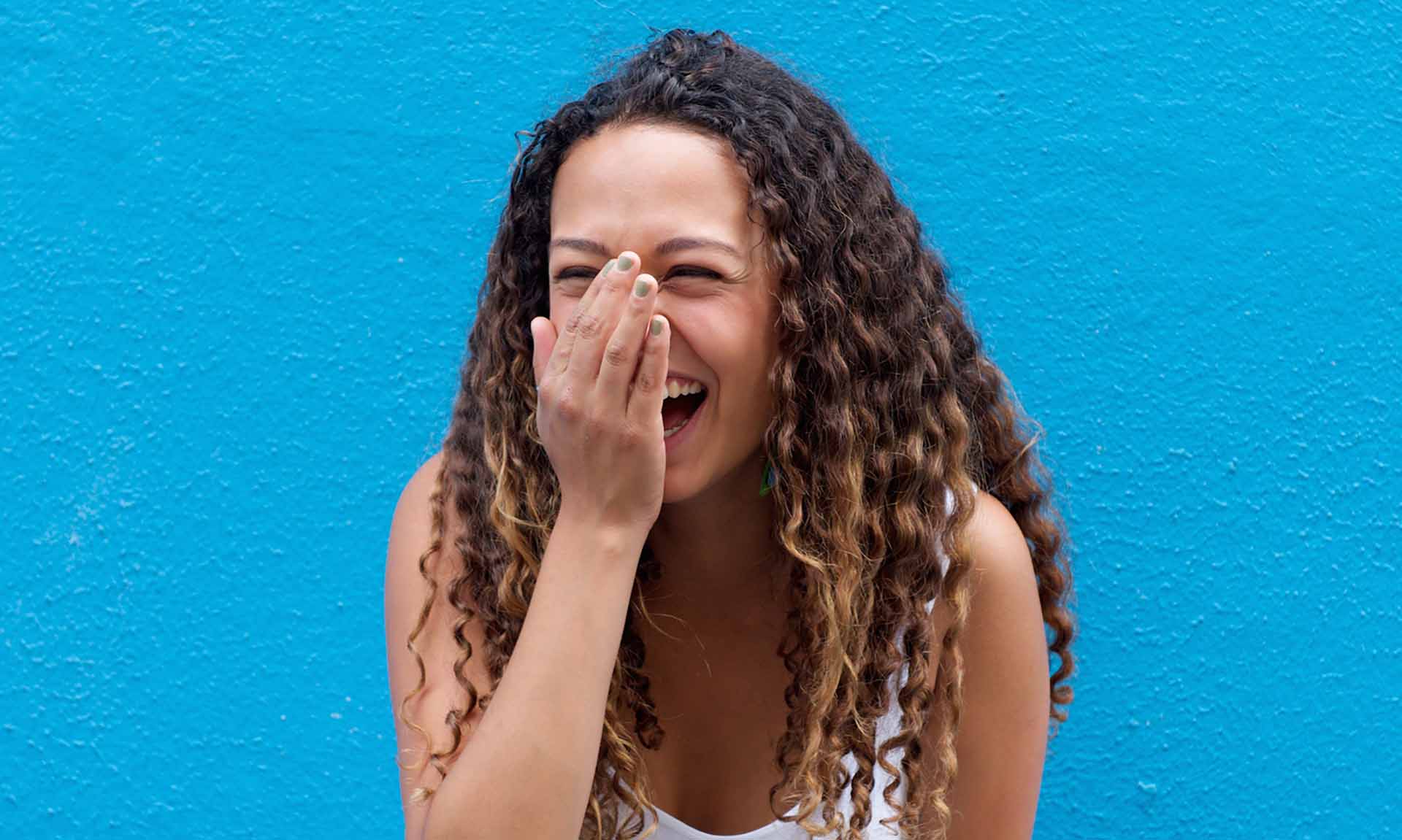 Portrait of young woman laughing standing against a blue wall