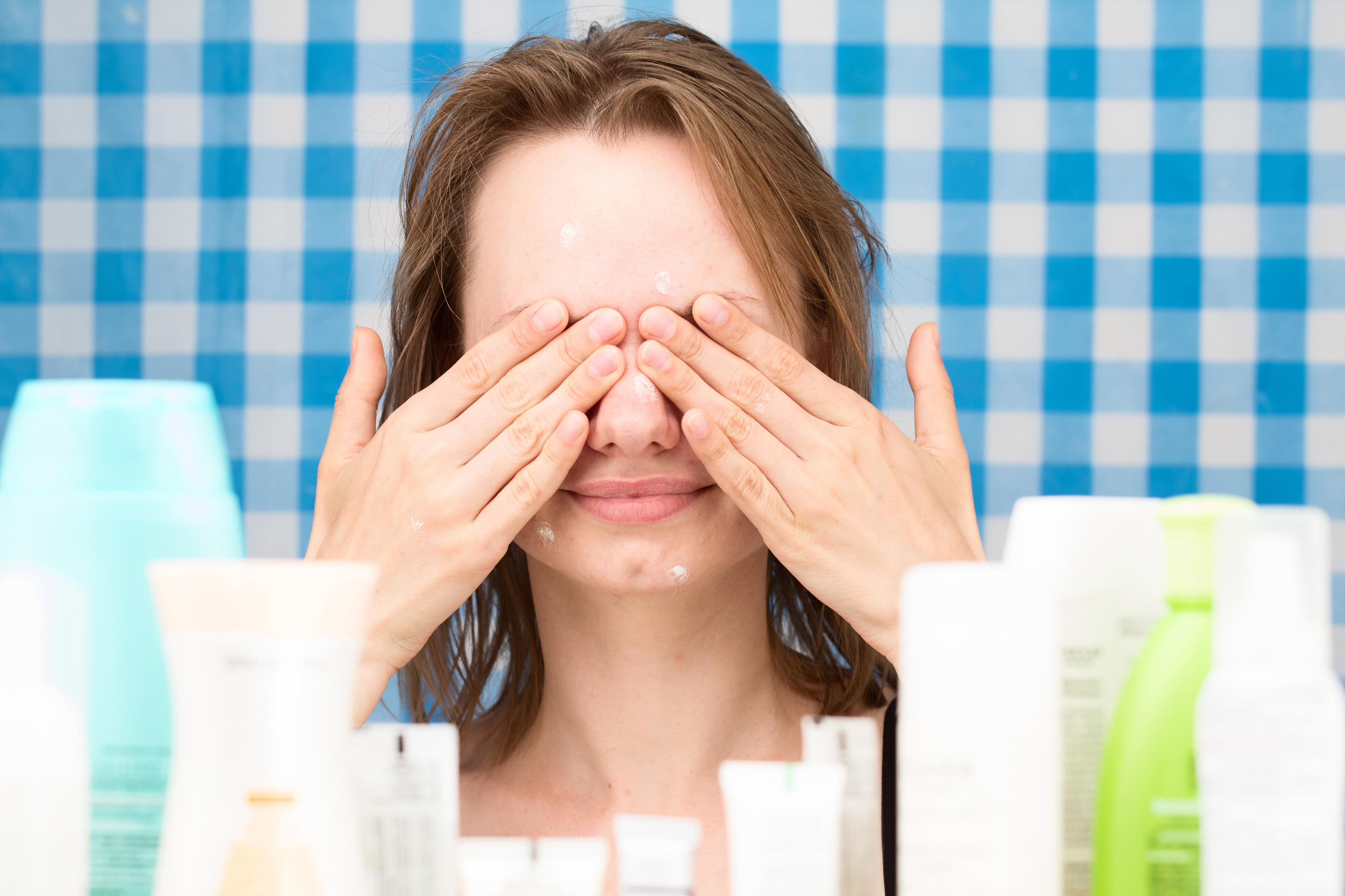 Young girl with problem skin is closed her eyes in front of set of cosmetics in bathroom. Skin care and beauty concept. Frontal portrait