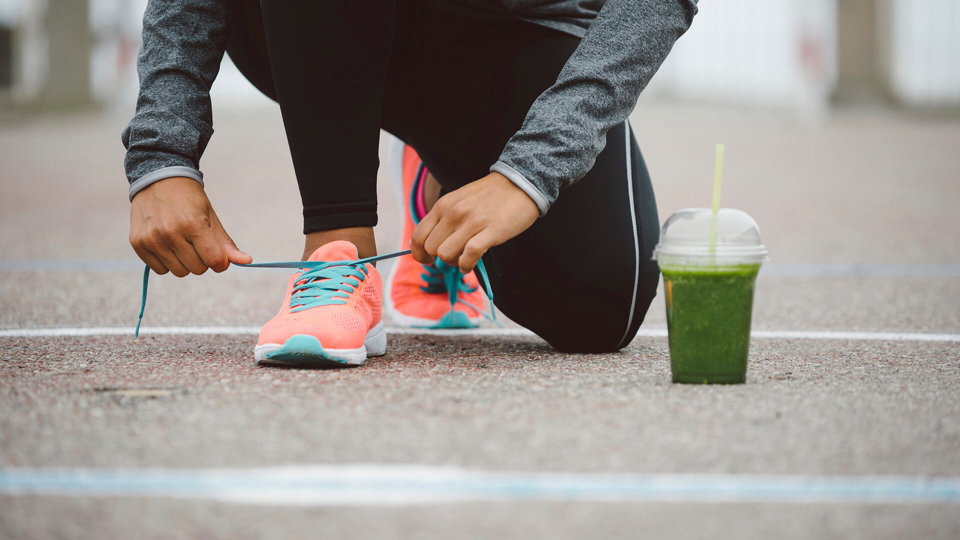 Fitness workout and healthy nutrition concept.  Detox smoothie drink and running footwear close up. Female athlete tying sport shoes laces before training outdoor.