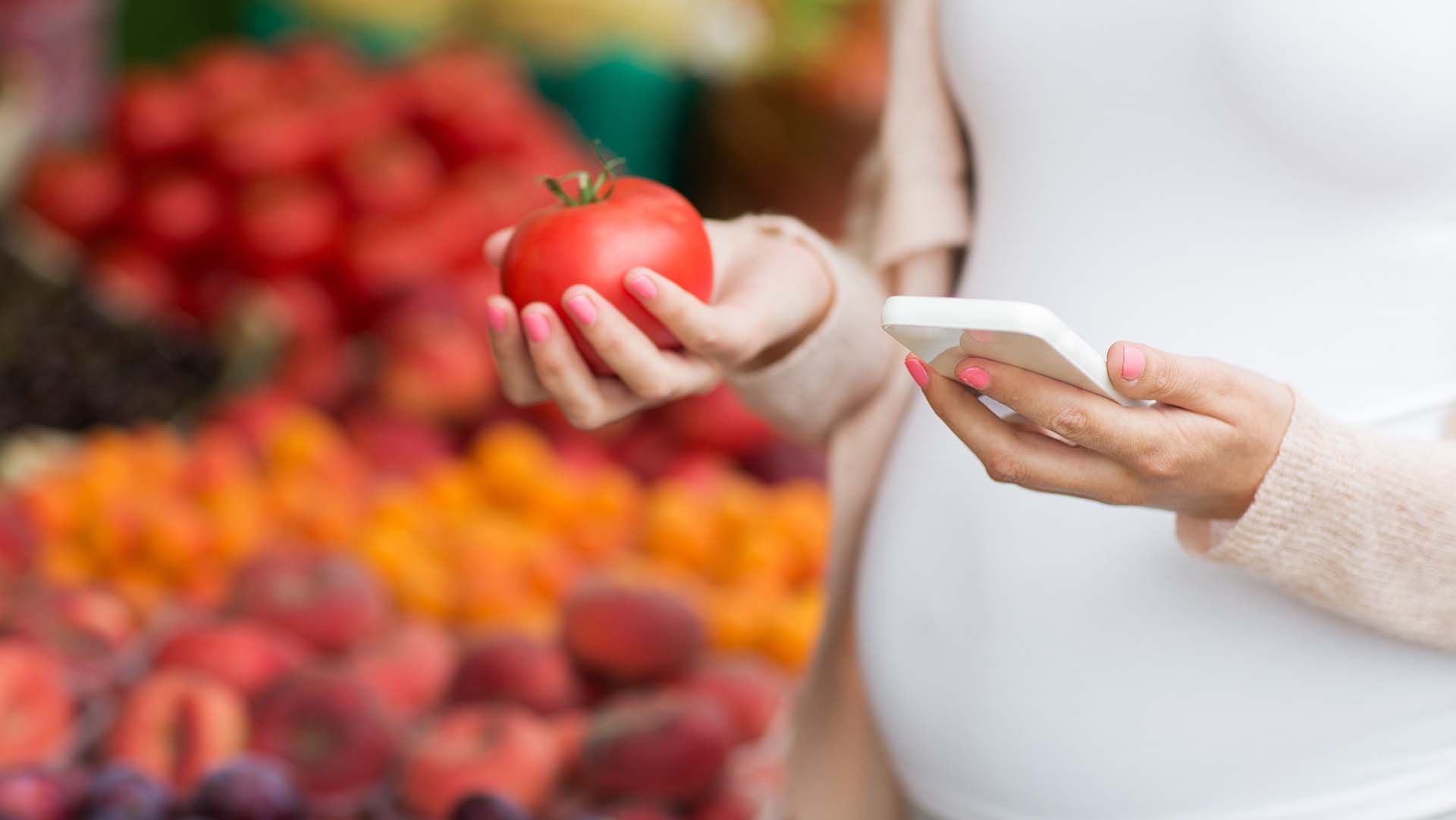 sale, shopping, food, pregnancy and people concept - close up of pregnant woman with smartphone and tomato choosing vegetables at street market