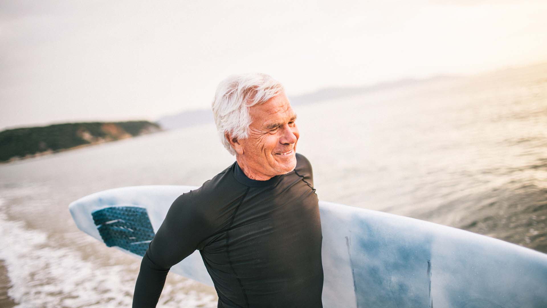 Portrait of a senior surfer holding his surfboard, being satisfied after a good surfing day