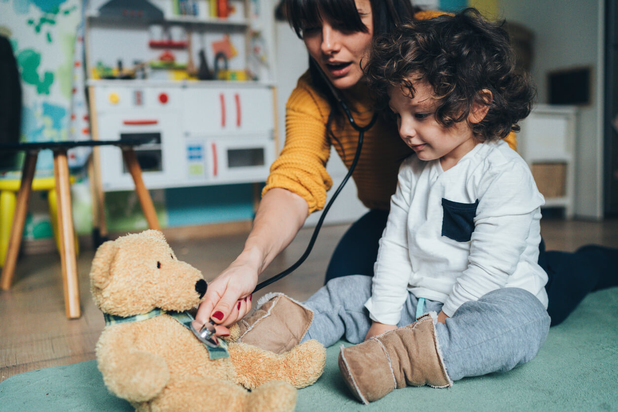 Woman and child holding stethoscope to teddy bear