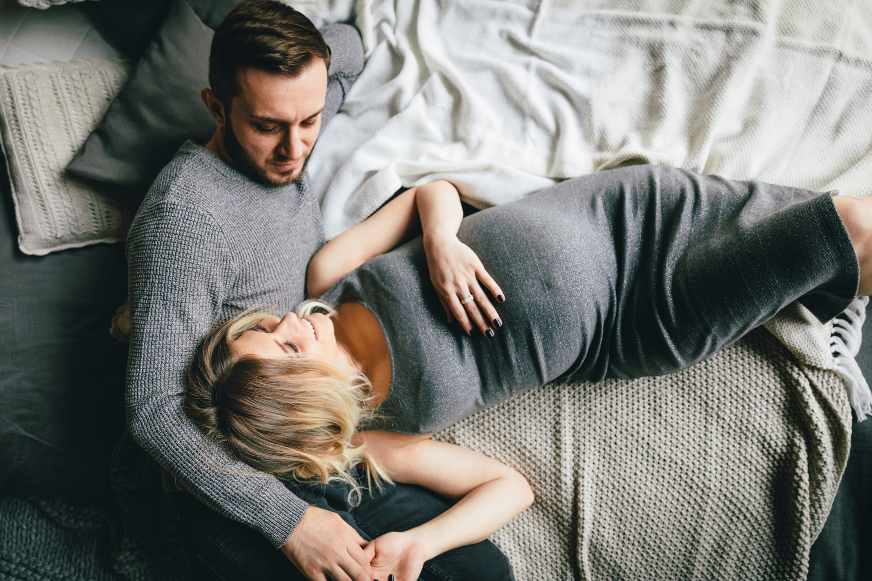 From above shot of young pregnant couple smiling while embracing on bed
