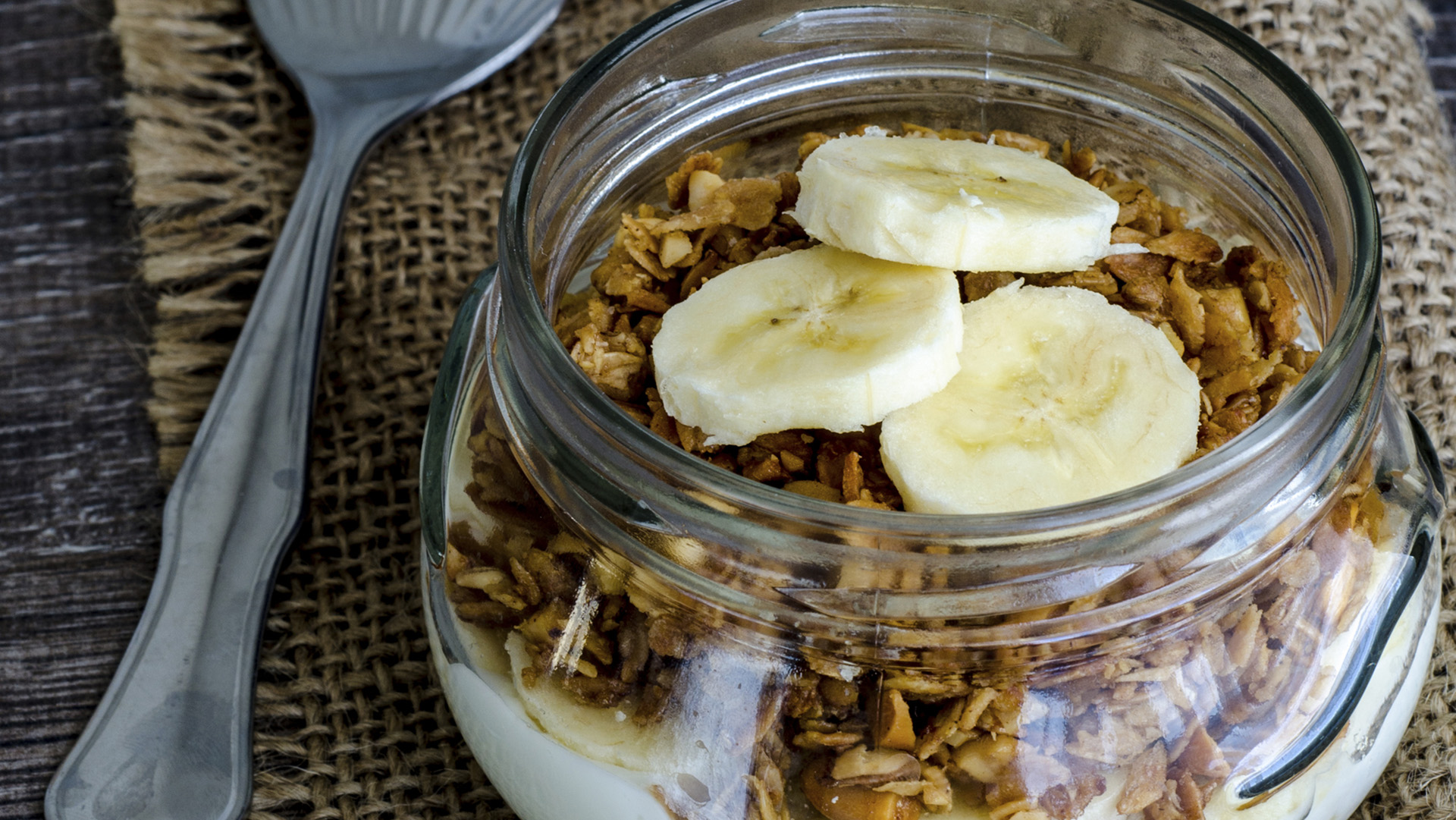 Healthy breakfast of granola, yoghurt and a banana in jar on rustic cloth