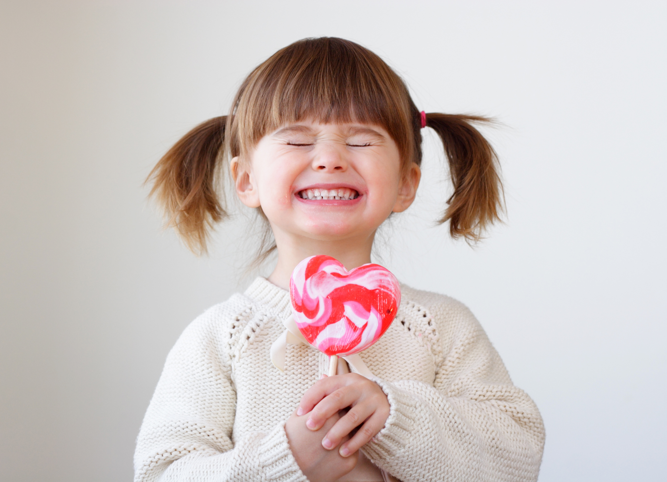 Beautiful little girl holding a big heart shaped lollipop