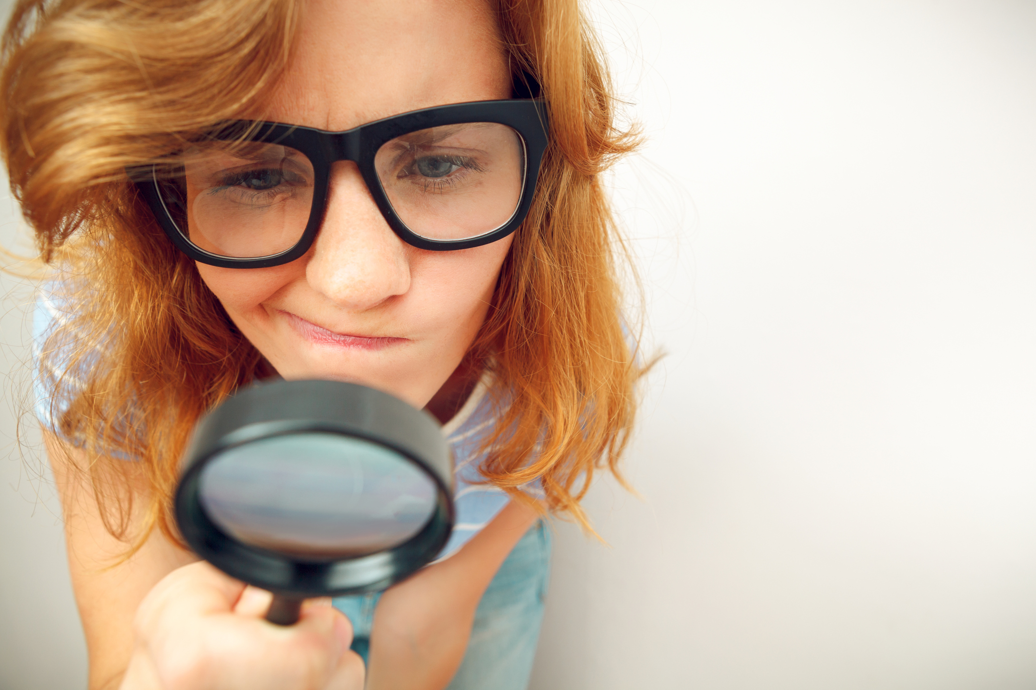 Young geek looking through magnifying glass.