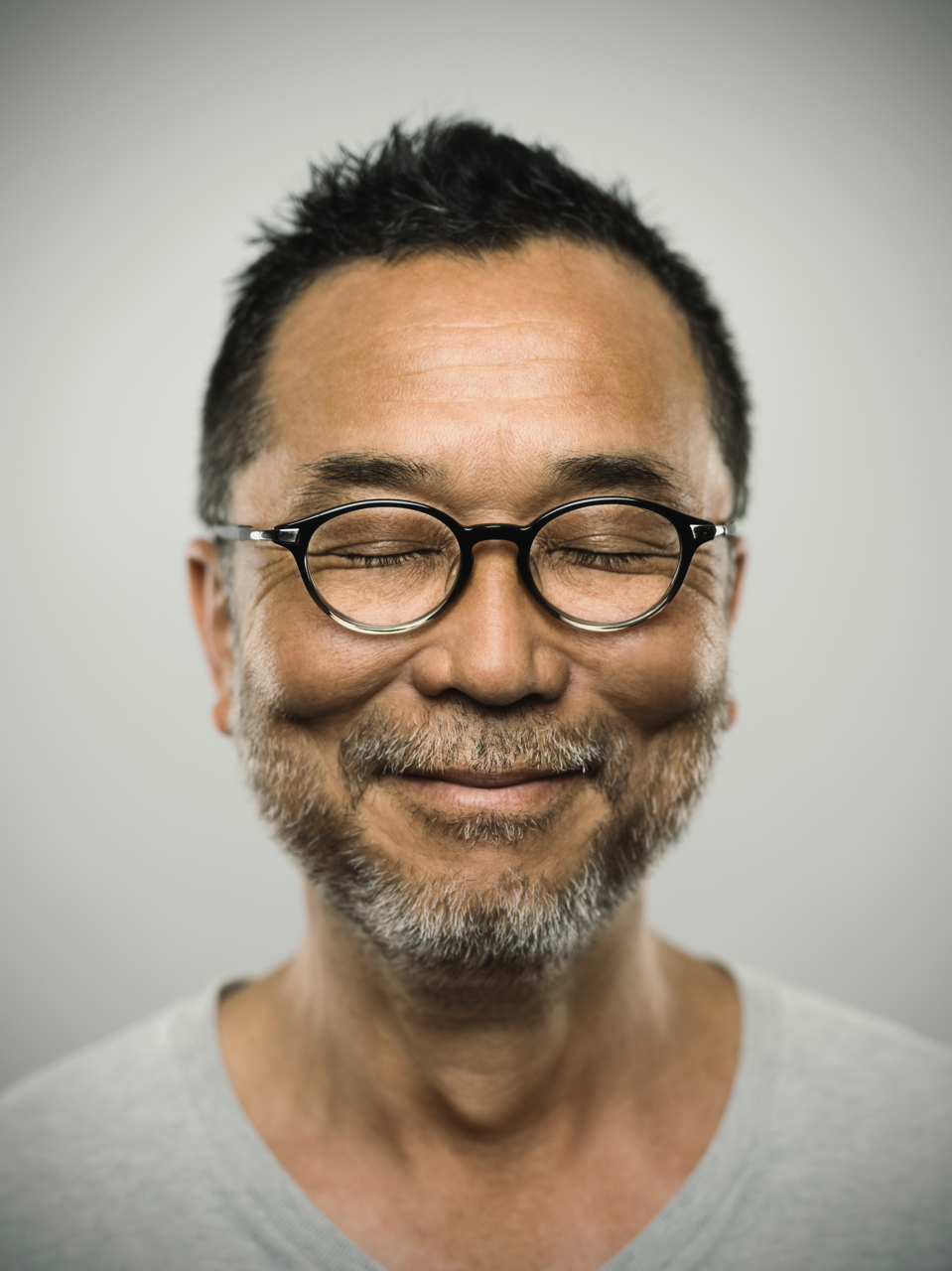 Studio portrait of a japanese mature man looking at camera with relaxed expression. The man has around 50 years and has glasses, short hair and a short grey beard. Vertical colour image from a medium format digital camera.