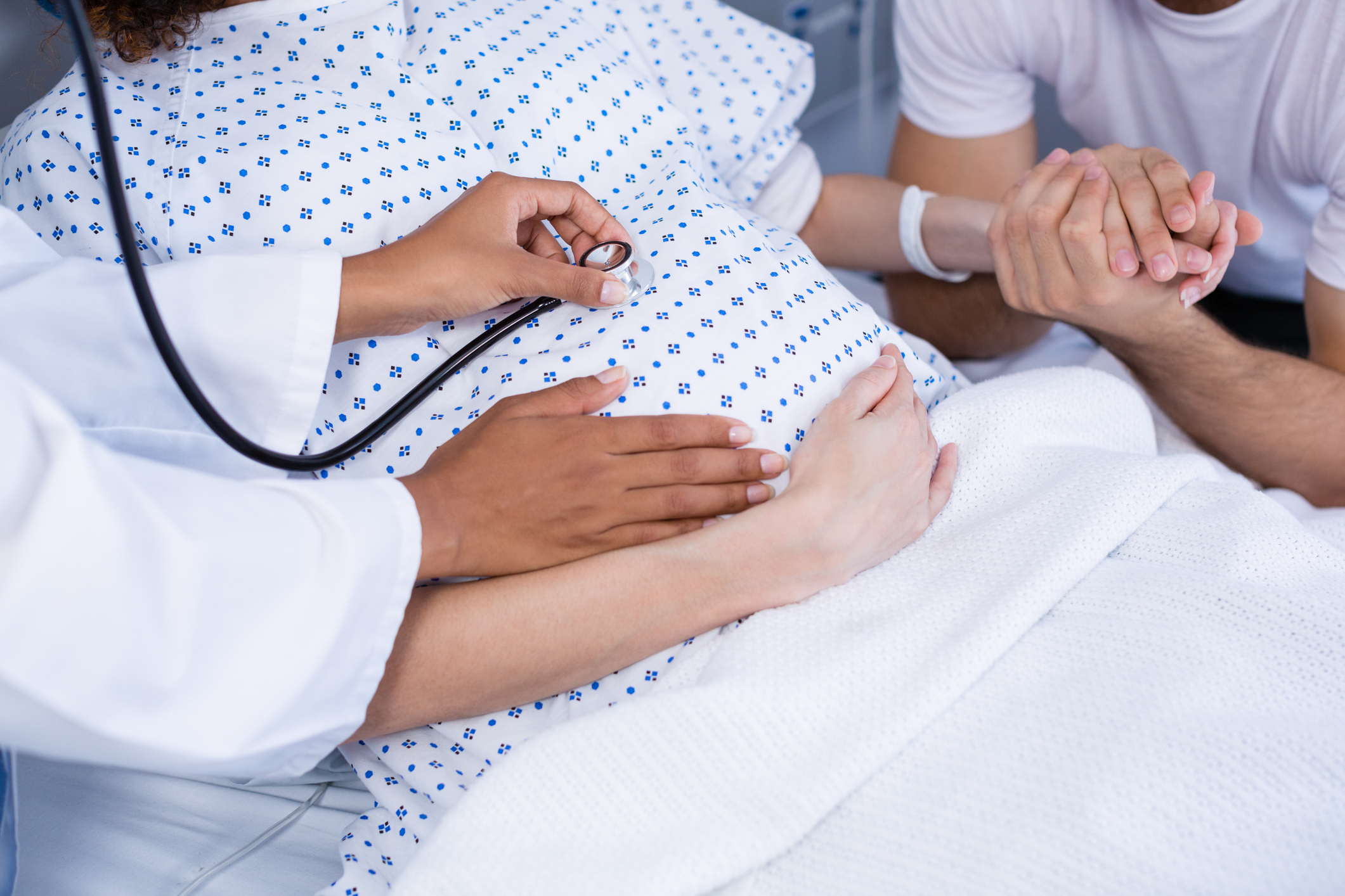 Doctor examining pregnant womans belly with stethoscope in ward of hospital