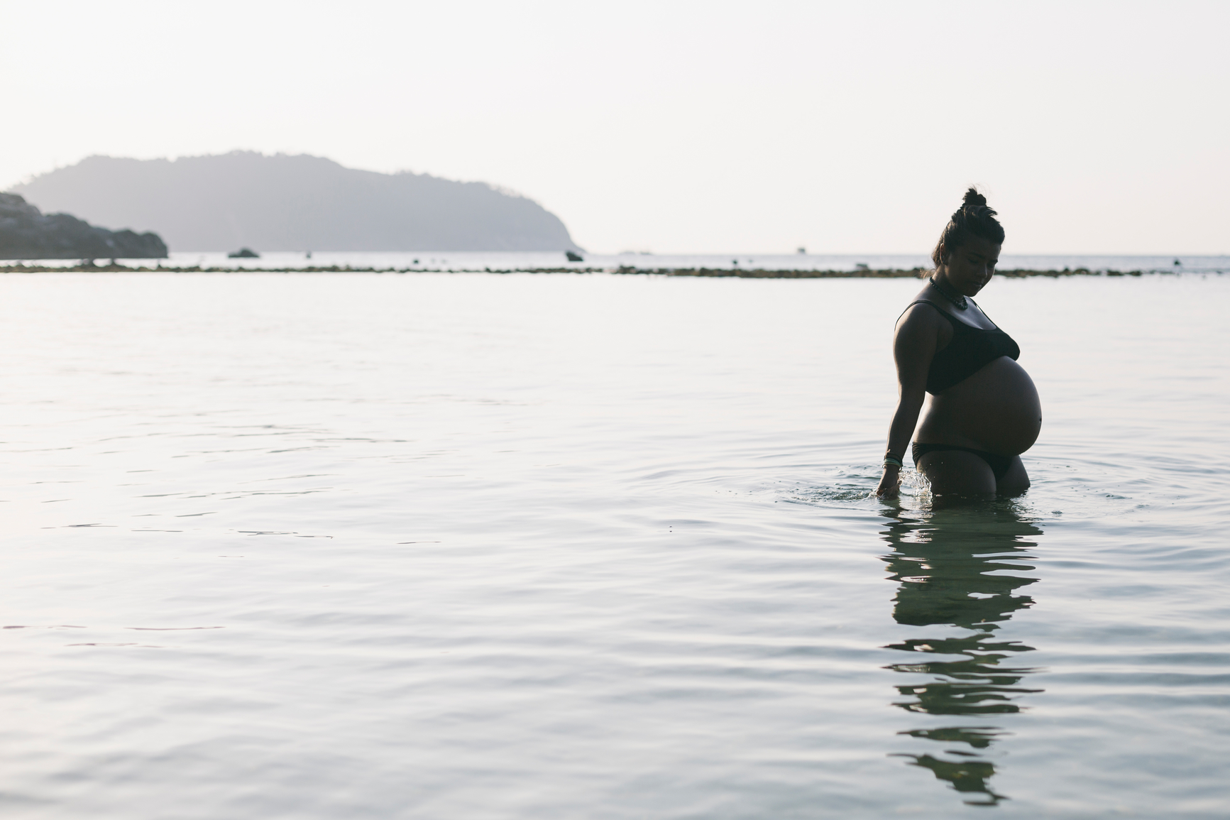 A Pregnant woman walks into the water at a tropical beach