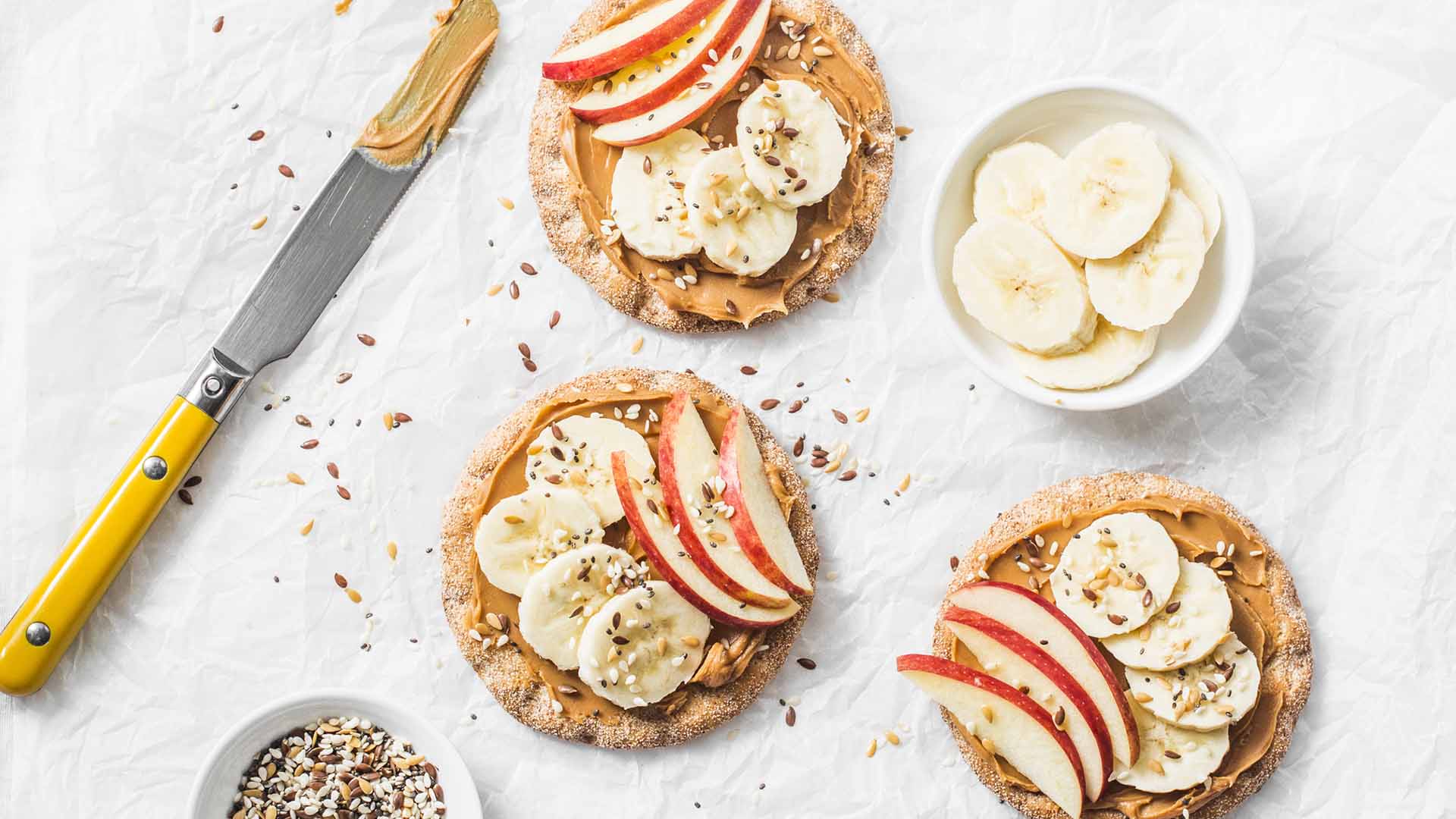 Peanut butter, apple, banana, flax and chia seed  crackers toast on a light background, top view
