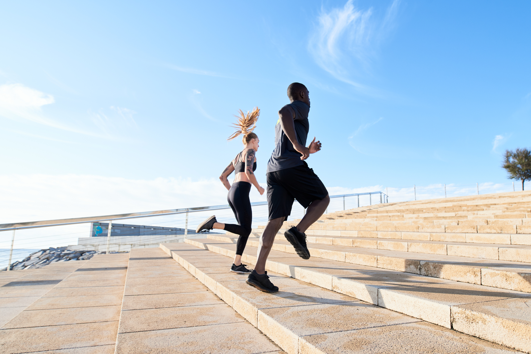 Two young people training together in seafront running up stairs in morning time.