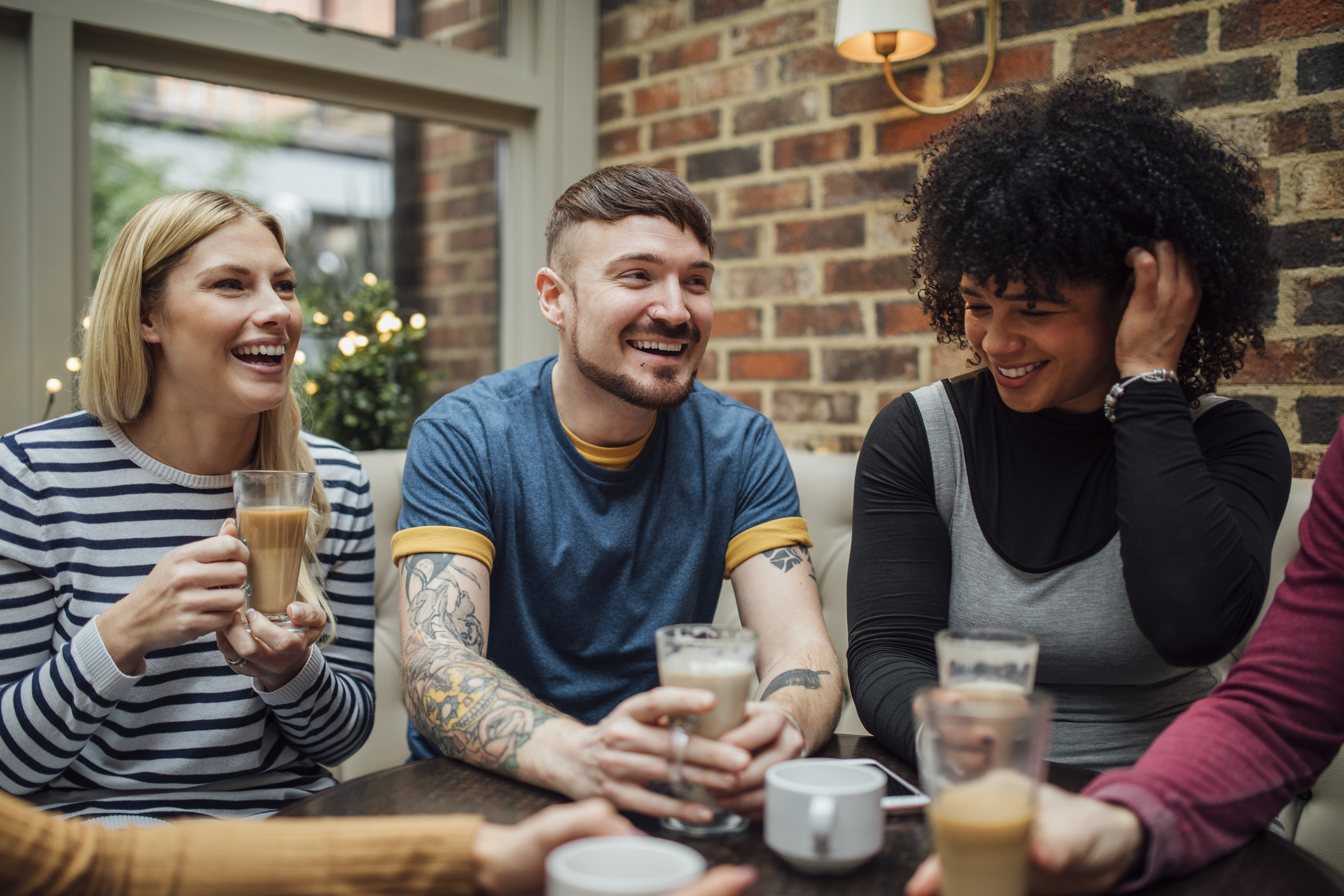 Friends are socialising over coffee in a coffee shop. They are laughing and talking with their drinks in their hands.