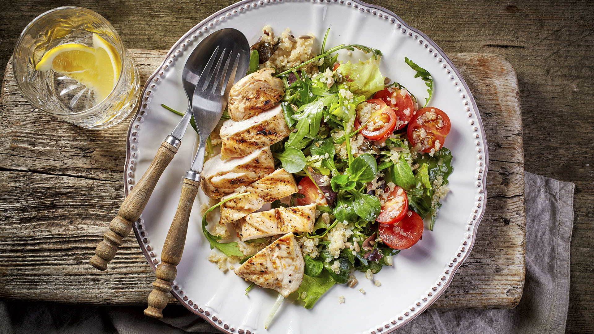 Quinoa and vegetable salad and grilled chicken fillet on white plate, top view