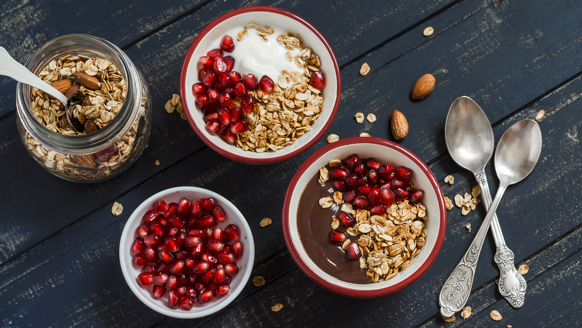 Healthy Breakfast - yogurt with homemade granola and pomegranate on a dark wooden board.