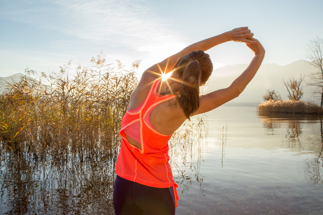 Beautiful and sporty young woman stretching after jogging outdoors. Arms outstretched above head.