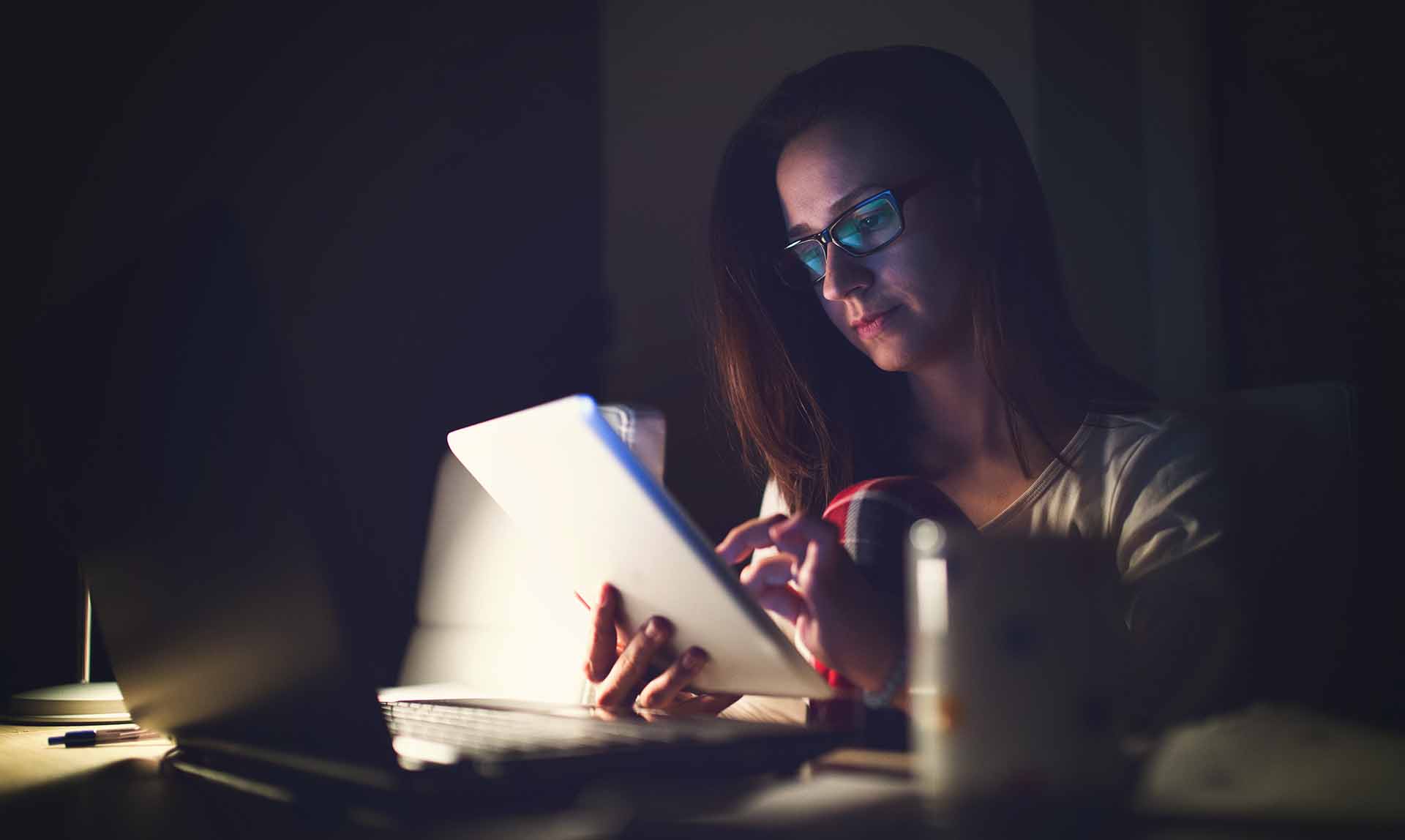 Young woman working late in front of a monitor.Businesswoman drinking coffee at his work place at night. Beautifil lady is surfing the internet late . Woman using tablet