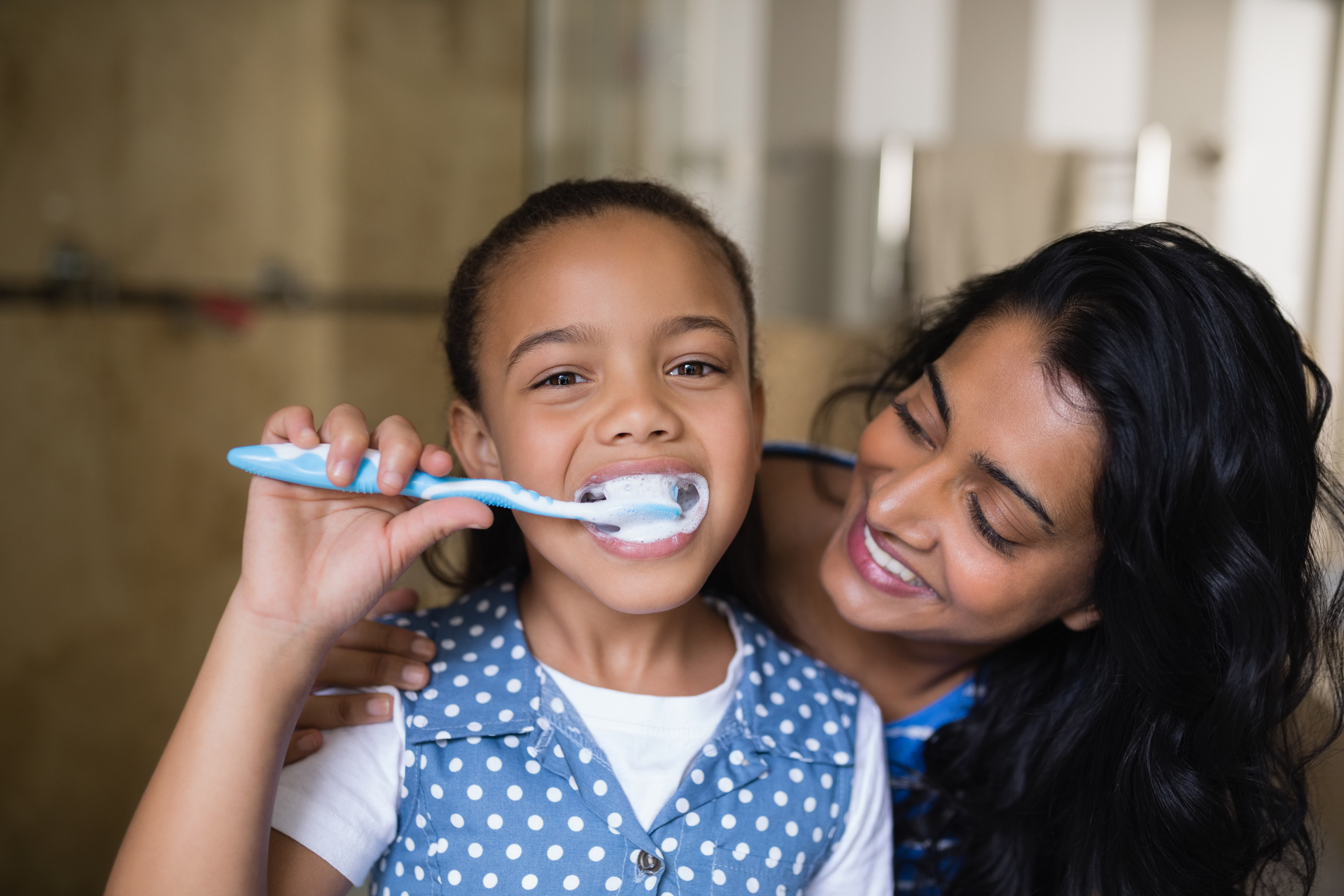 Close up portrait of girl brushing teeth with mother in bathroom