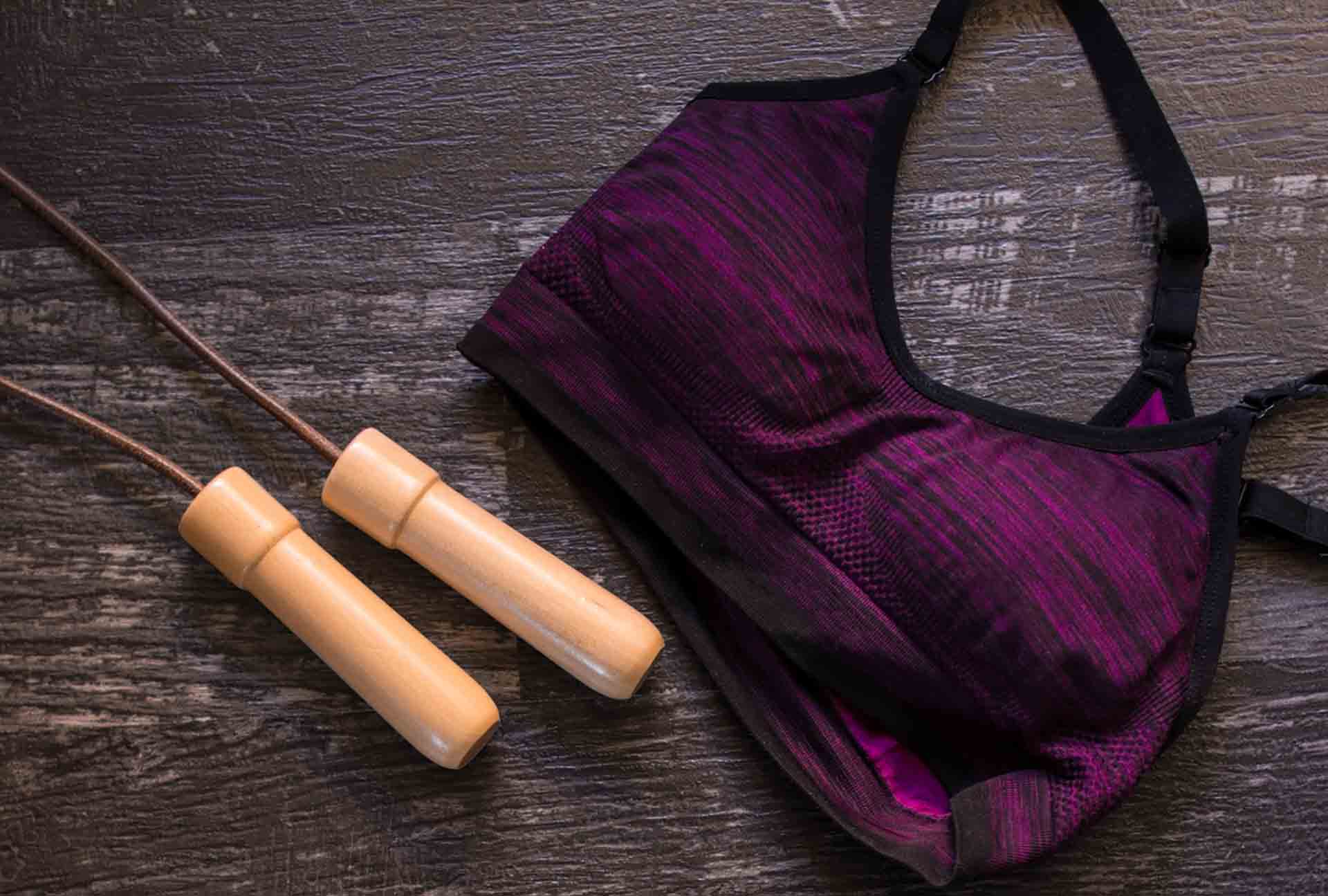 Closeup top view shot of sport bra and a jumping rope aside an exercise mat on a dark wooden floor background. Copy space