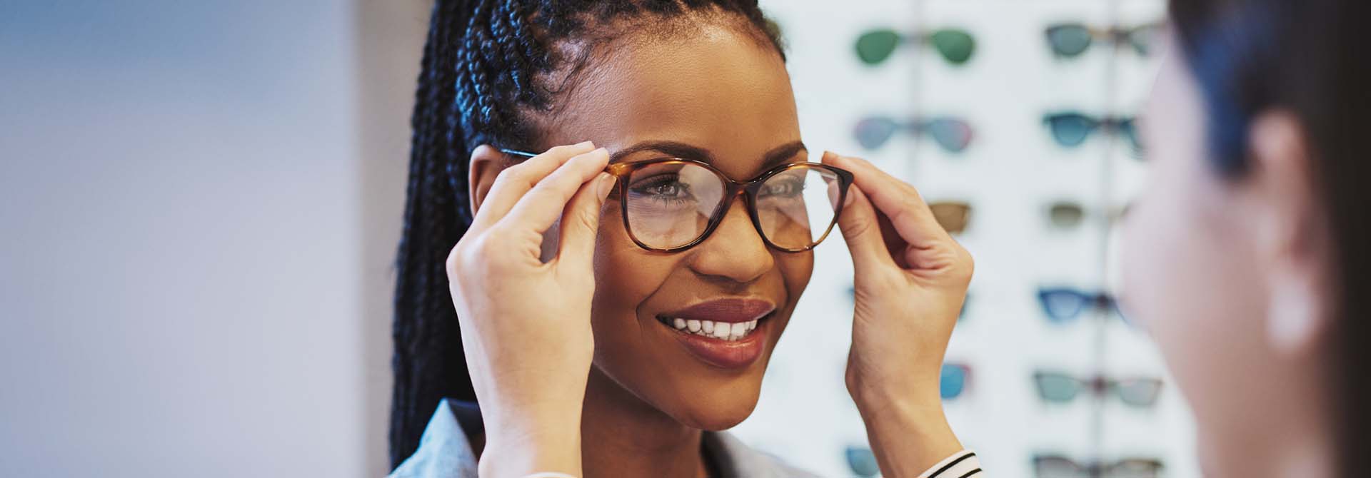 Attractive young African woman selecting glasses with the help of an optometrist in a store trying on different frames