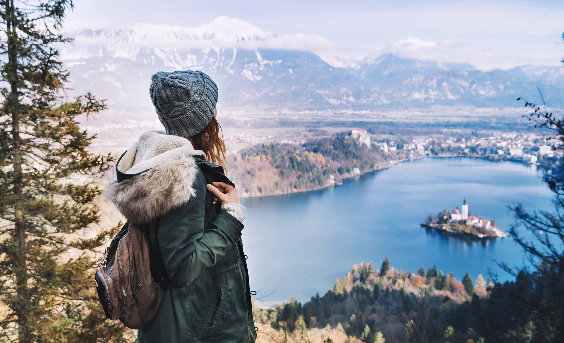 Hiking young woman with alps mountains and alpine lake on background. Travel Slovenia, Europe. Top view on Island with Catholic Church in Bled Lake with Castle and Mountains in Background.