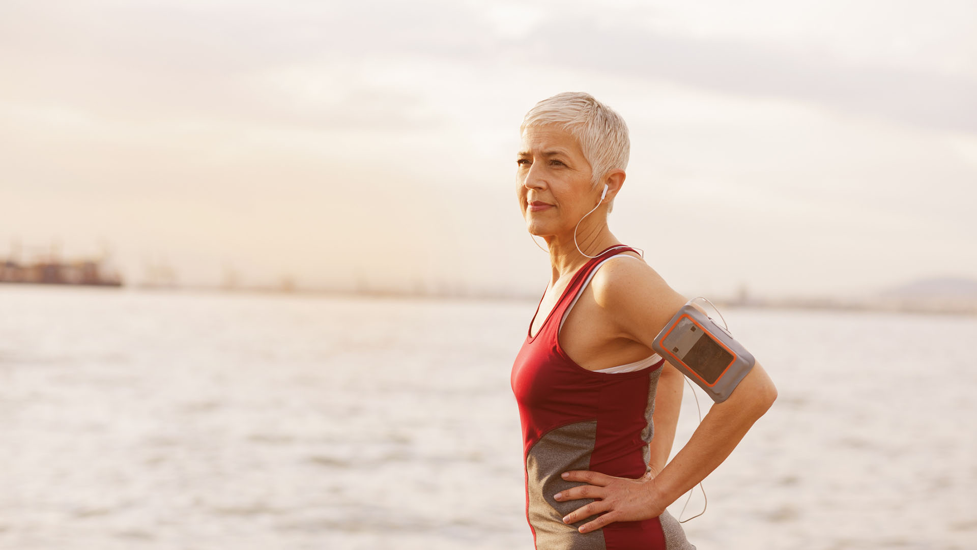 Mature-senior woman jogging at the coast, she using mobile phone