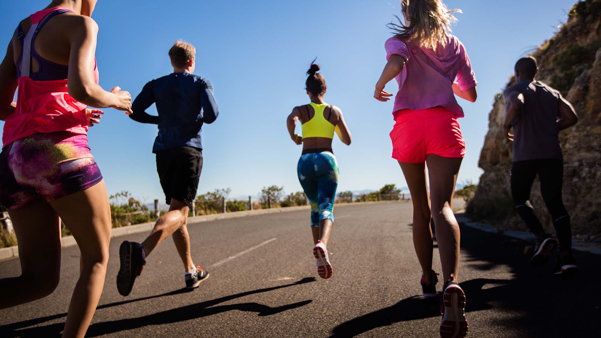 Multi-ethnic group of young adult athletes wearing sports clothing running outdoors on summer