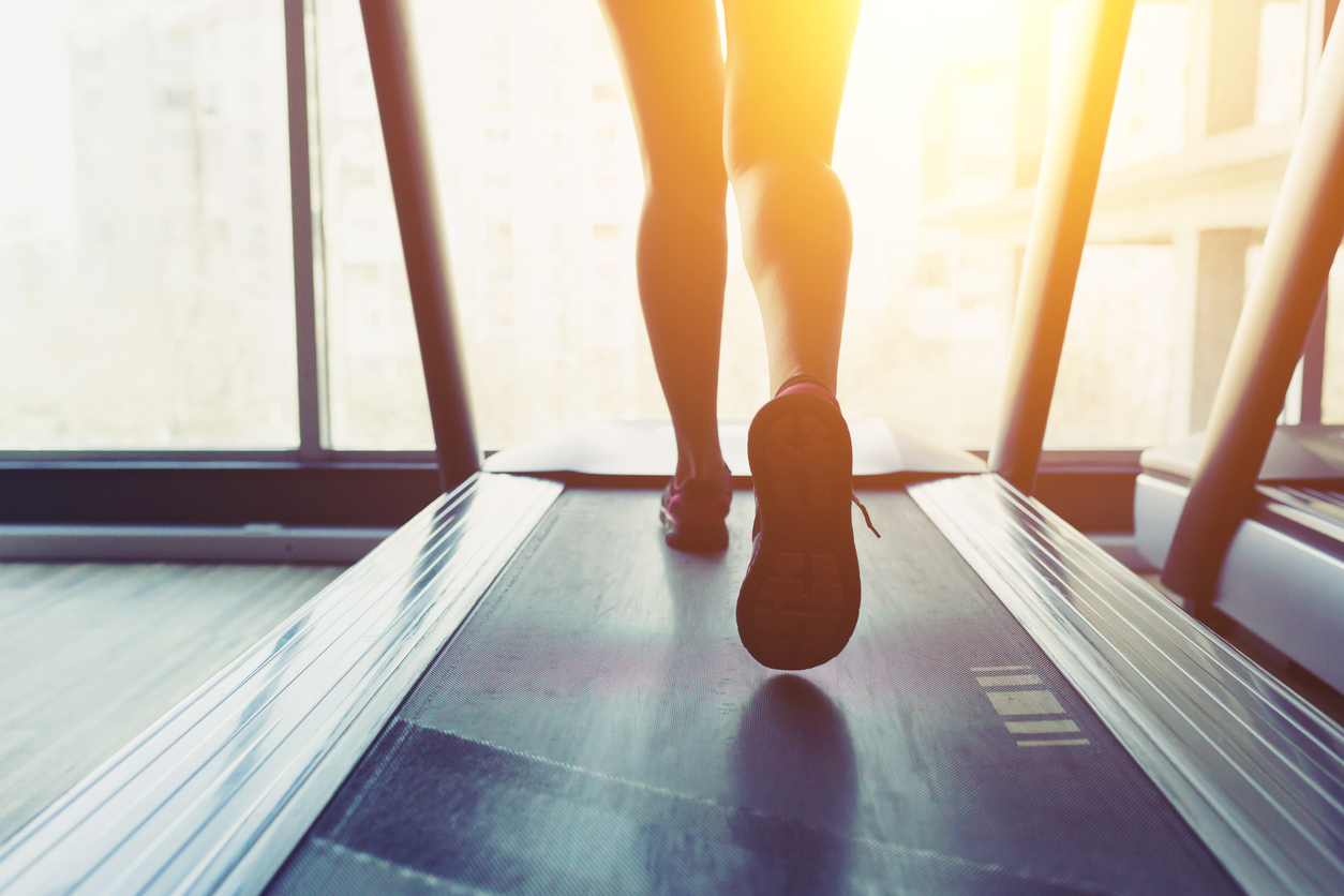 Fitness girl running on treadmill. Woman with muscular legs in gym