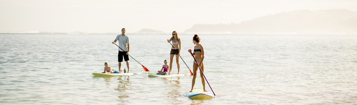 A multi-ethnic family on vacation in the ocean stand up paddle boarding together on a sunny day in Hawaii.