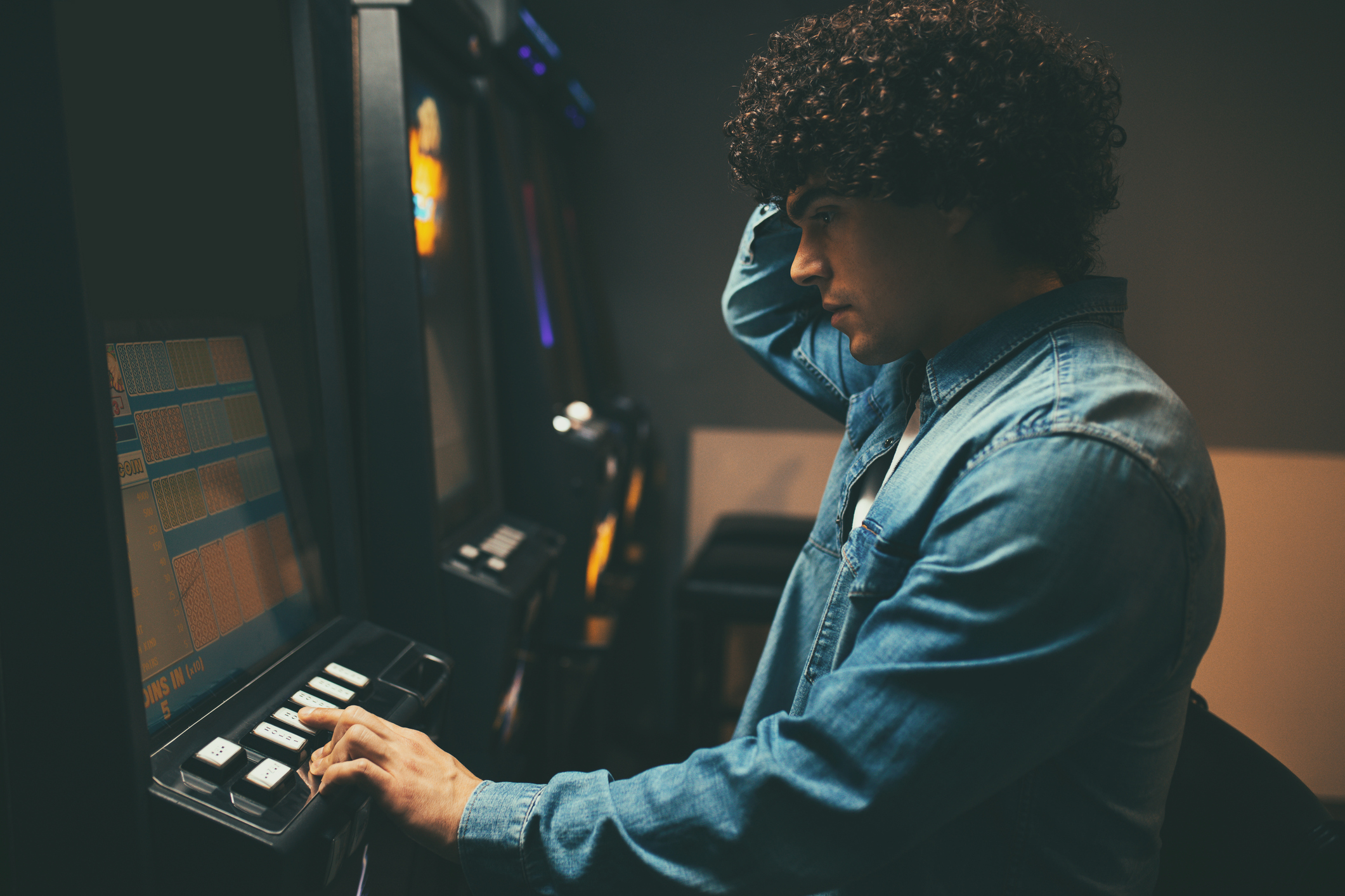 Worried man loosing his money on a slot machine in a casino.