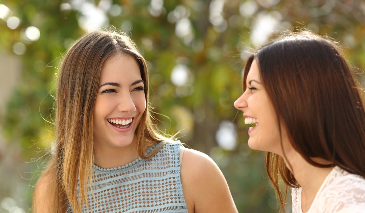 Happy women talking and laughing in a park with a green background