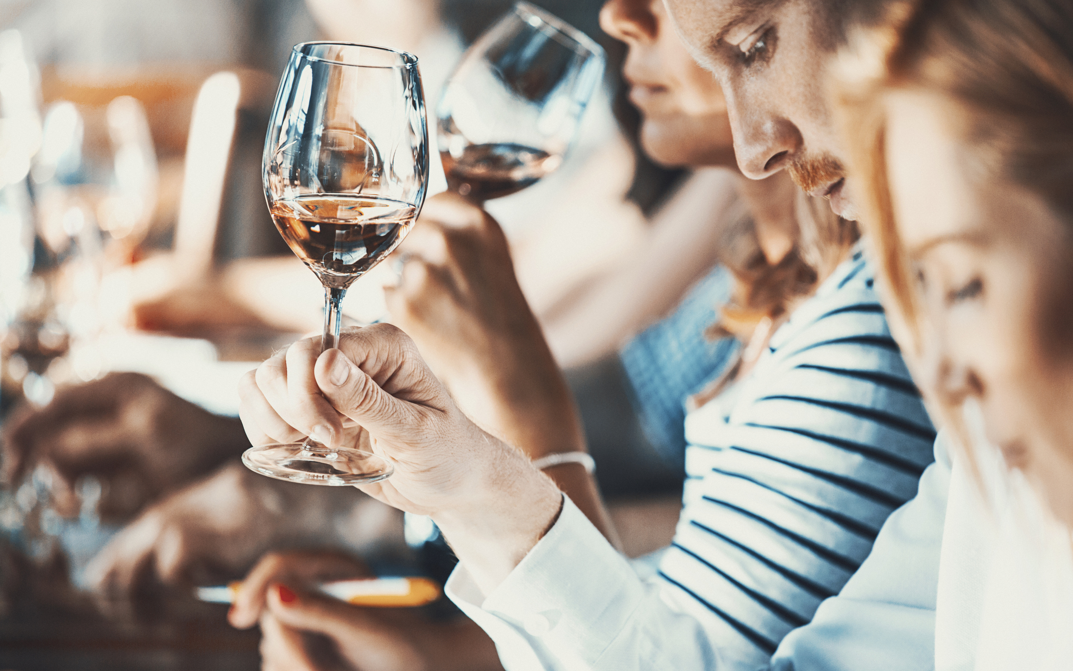 Closeup side view of group of adults tasting different wines at a local winery. They are using wine charts and writing down their impressions. There are two men and two women.