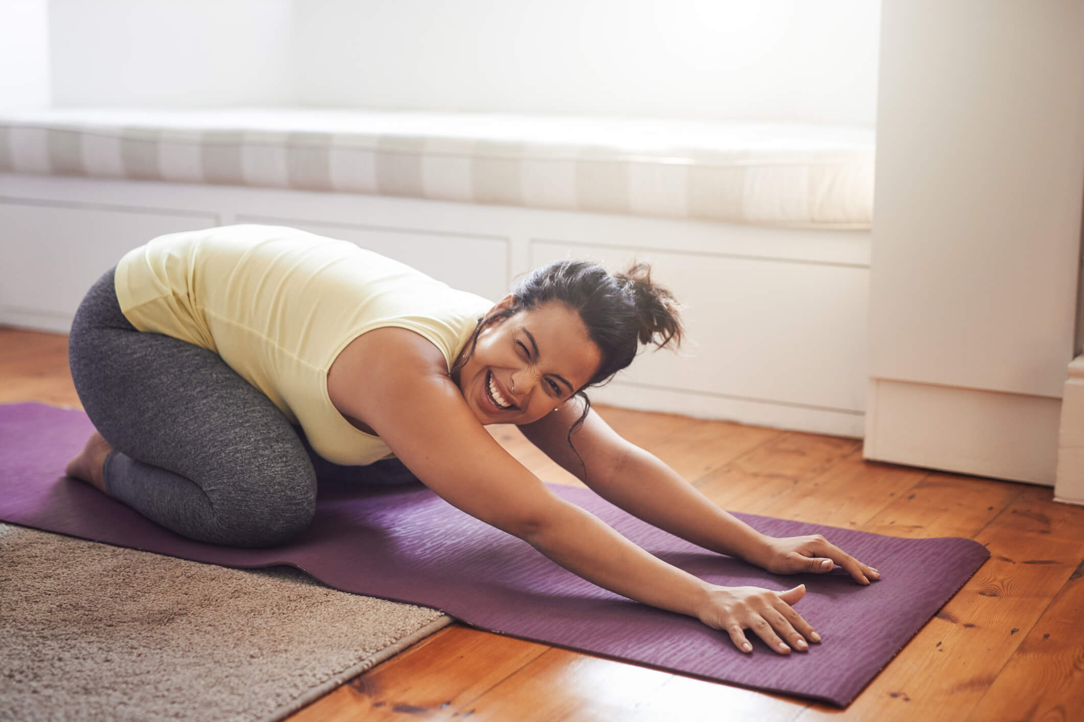 A young woman in workout gear stretches out on a purple yoga mat.