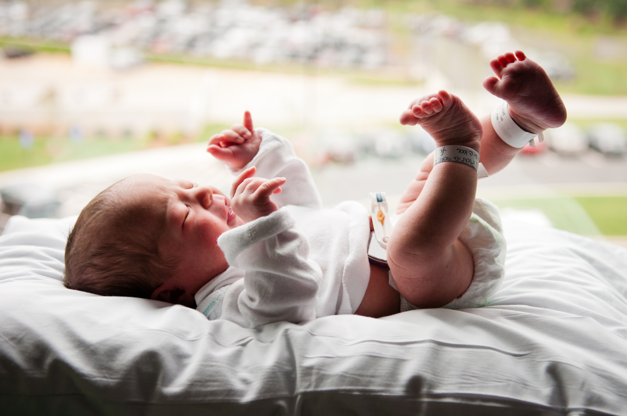 A new born baby girl laying by the window in front of a parking lot with an alarm system attached to the umbilical cord.