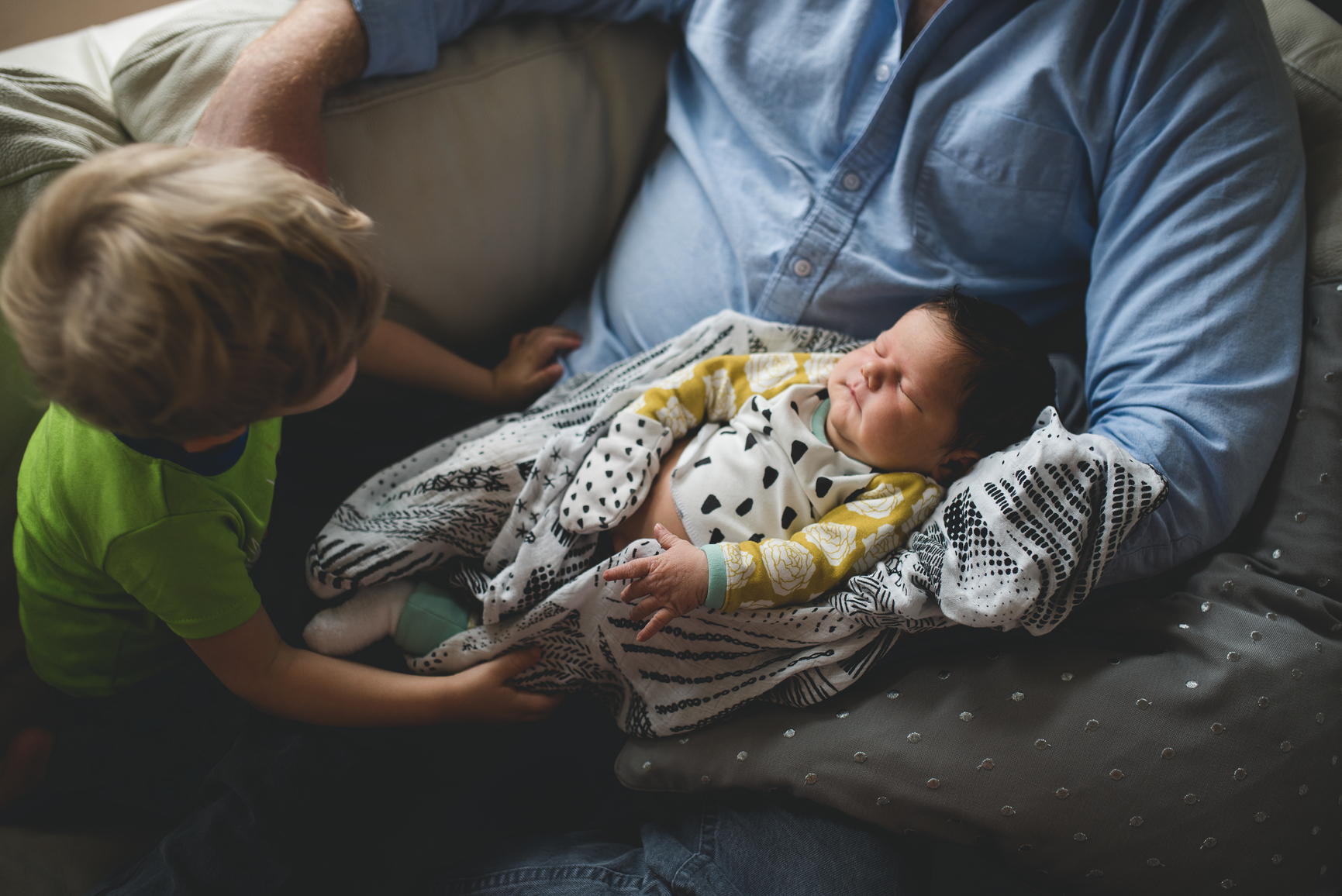 toddler son looking at newborn baby in dad's lap