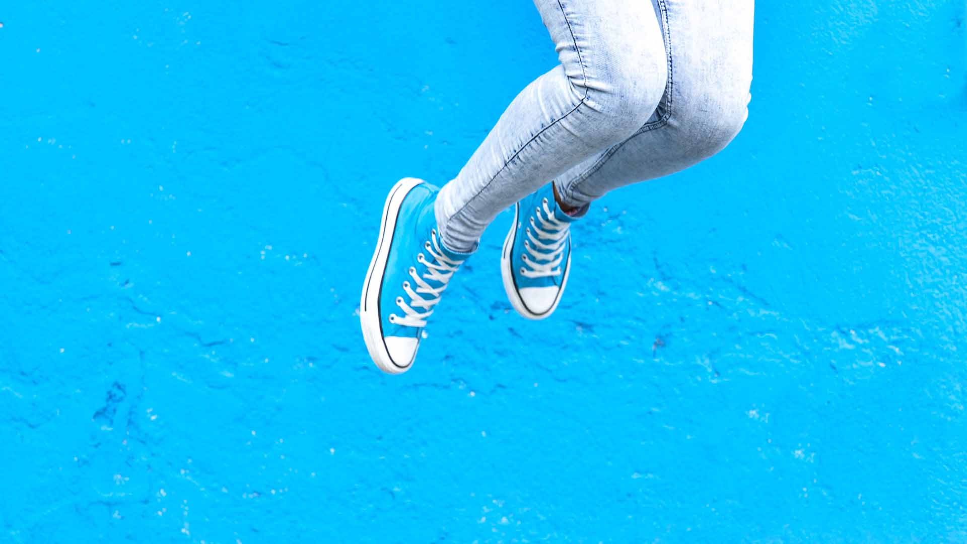 Jumping woman legs in blue sneakers against  blue wall background