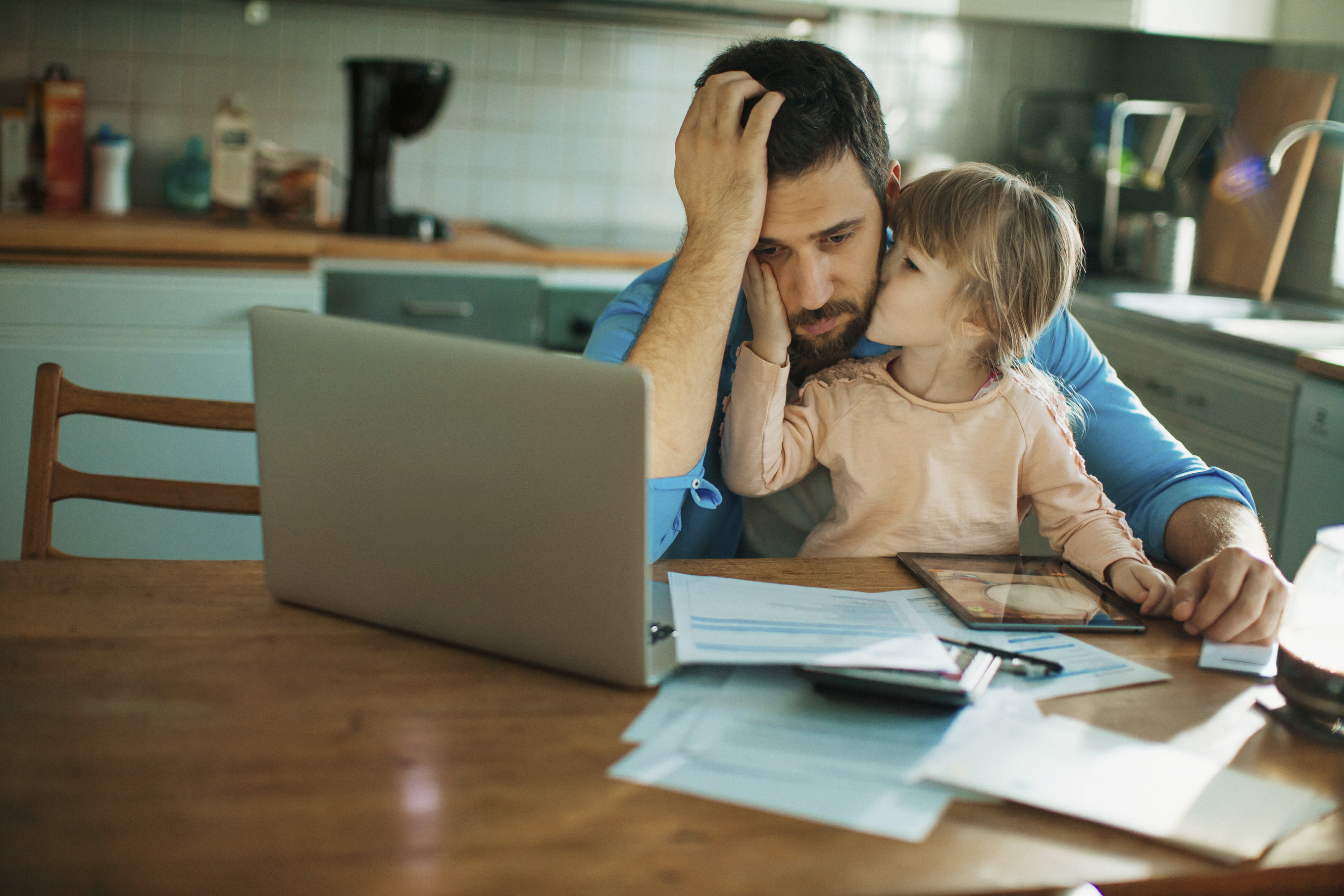 Photo of a father and daughter sitting in the kitchen,daughter is comforting her father who is worried about home bills