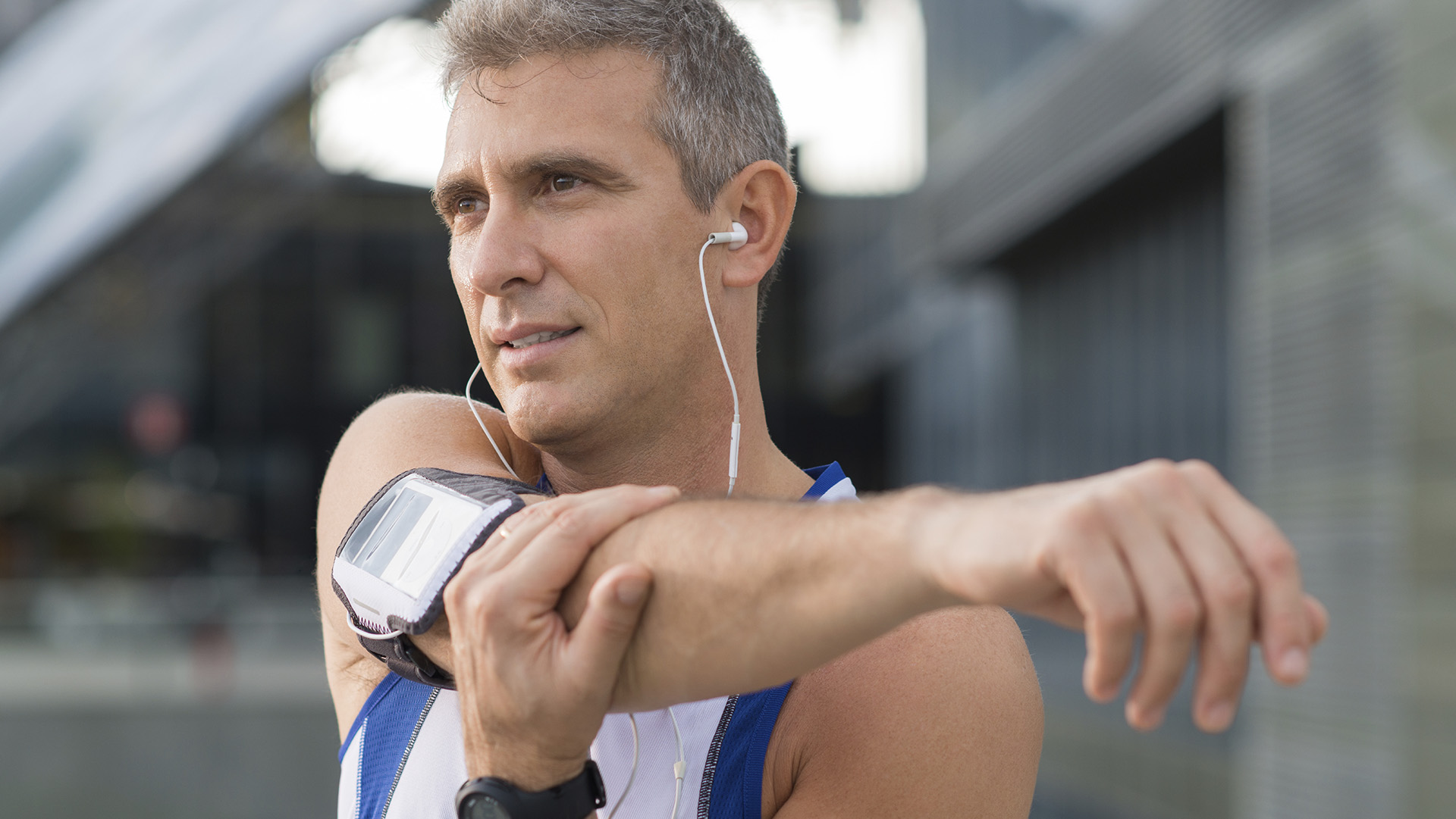 Mature Male Athlete Stretching And Listening To Music Outside
