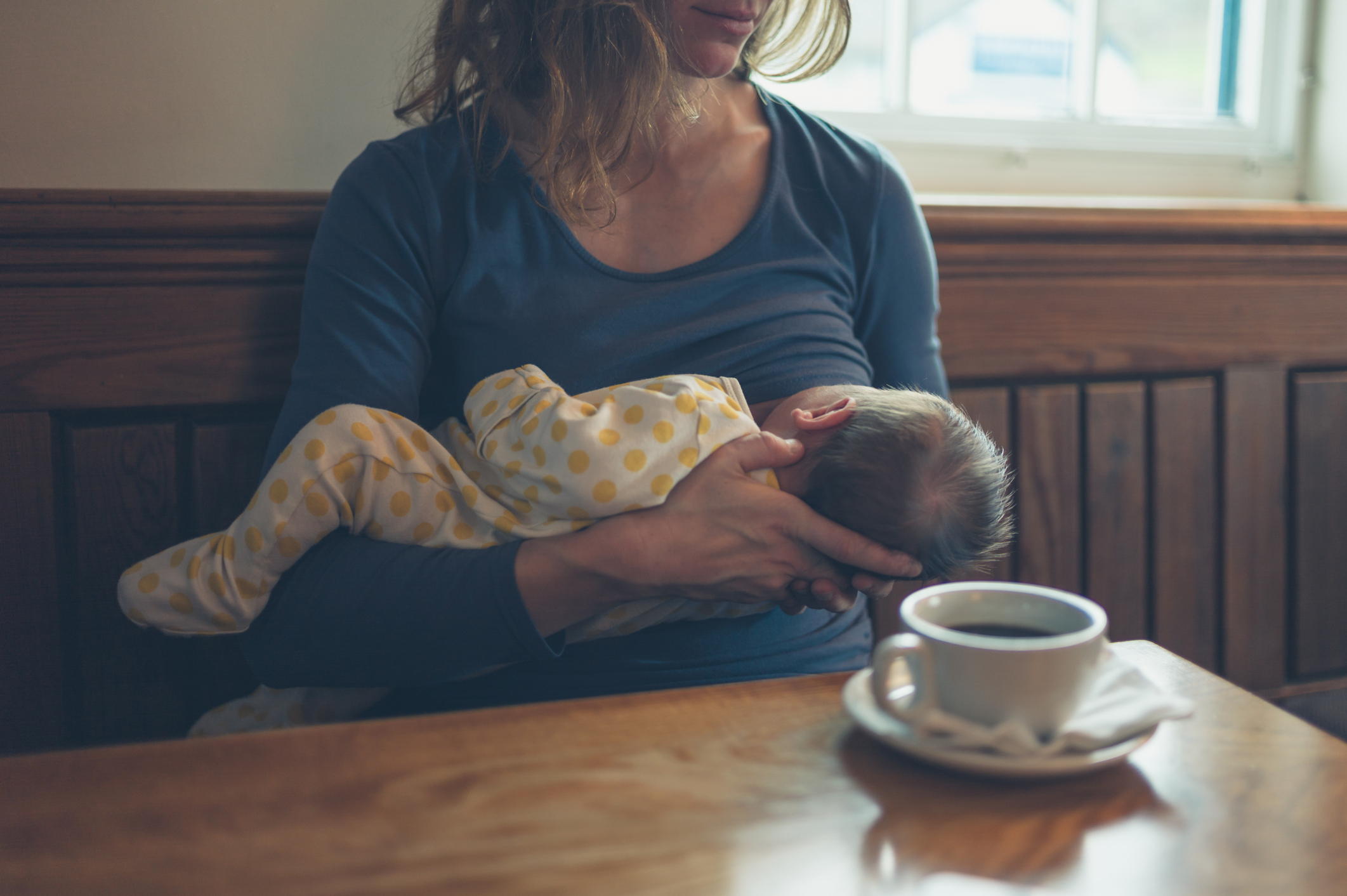 A young mother is breastfeeding her baby in a cafe while she is having a coffee