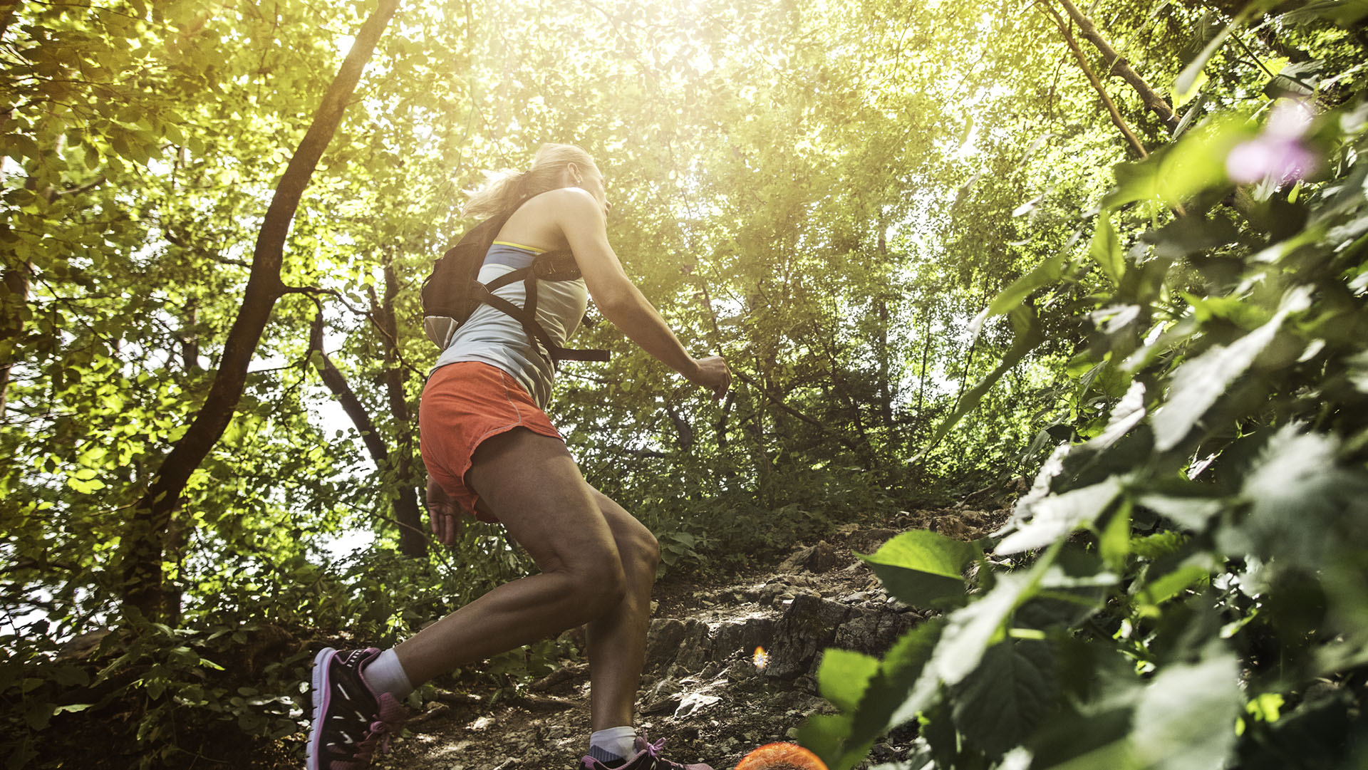Female runner going uphill on a rocky forest path.