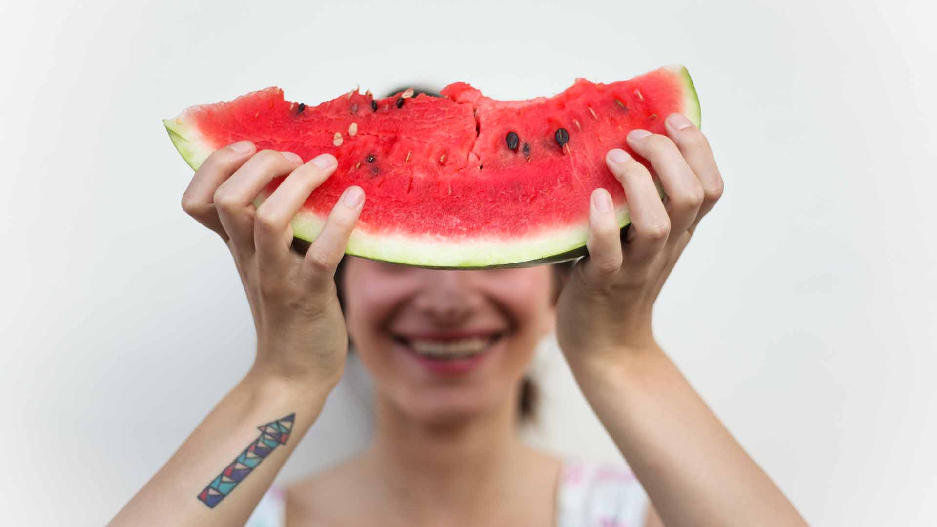 Woman holding a slice of watermelon in front of her face