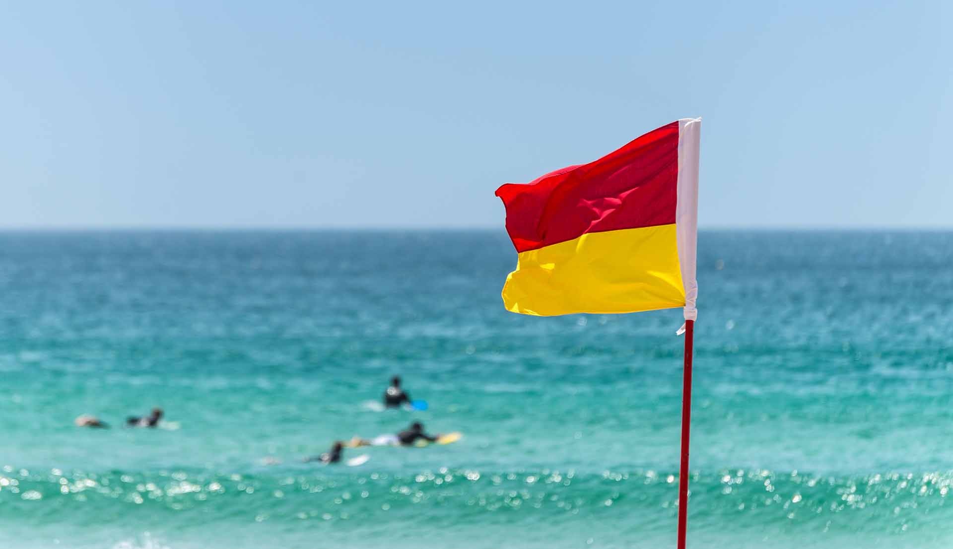 Red and yellow flag marking the limit of the safe swimming area on a beach under a blue summer sky