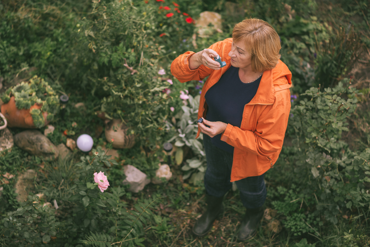 Senior woman in her 60s inhaling asthmatic cure while working in the garden. Woman is living life with chronic illness everyday and overcoming challenges that illness brings.