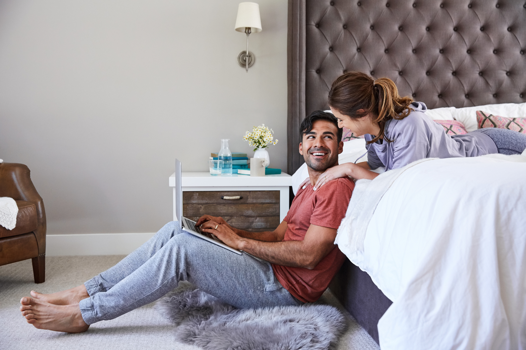 Millennial couple leisurely working on the computer in their bedroom after waking up in the morning