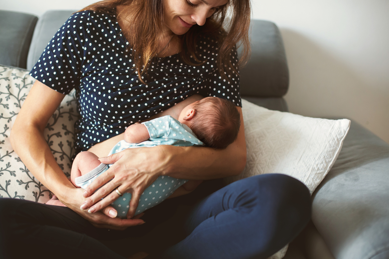 Young mother breastfeeds her baby, holding him in her arms and smiling from happiness