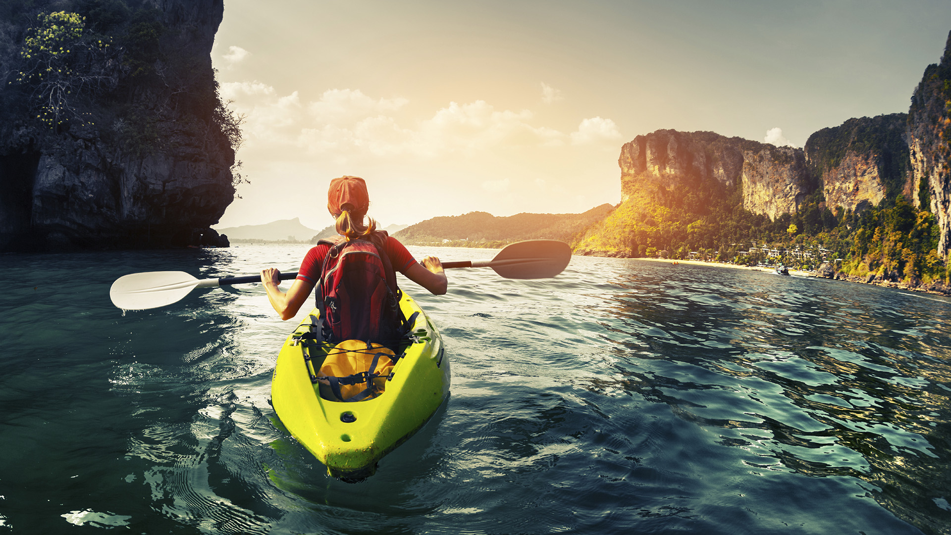 Lady paddling the kayak in the calm tropical bay at sunset