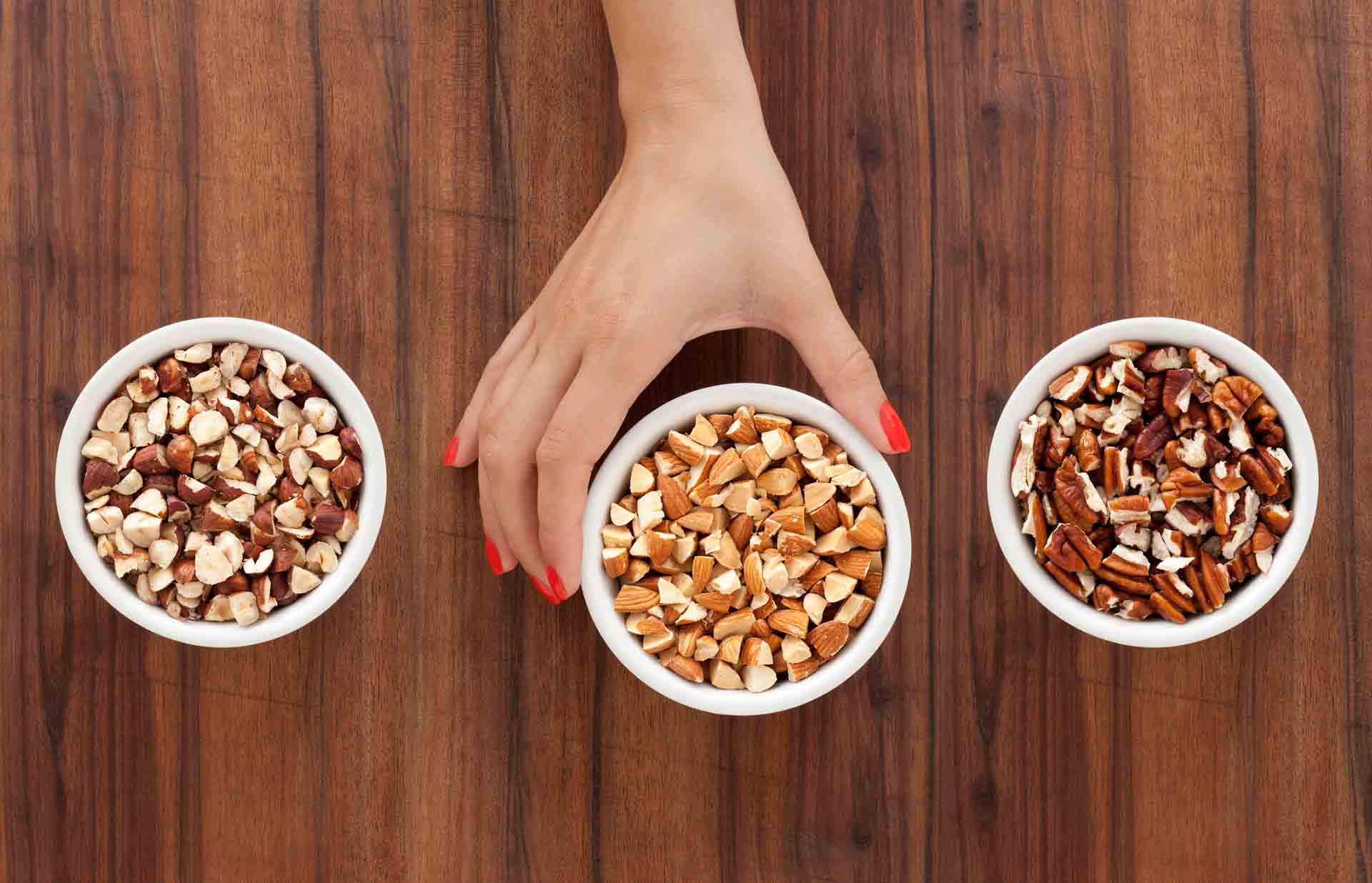 Three bowls with varieties of chopped nuts and woman's hand holding the middle one