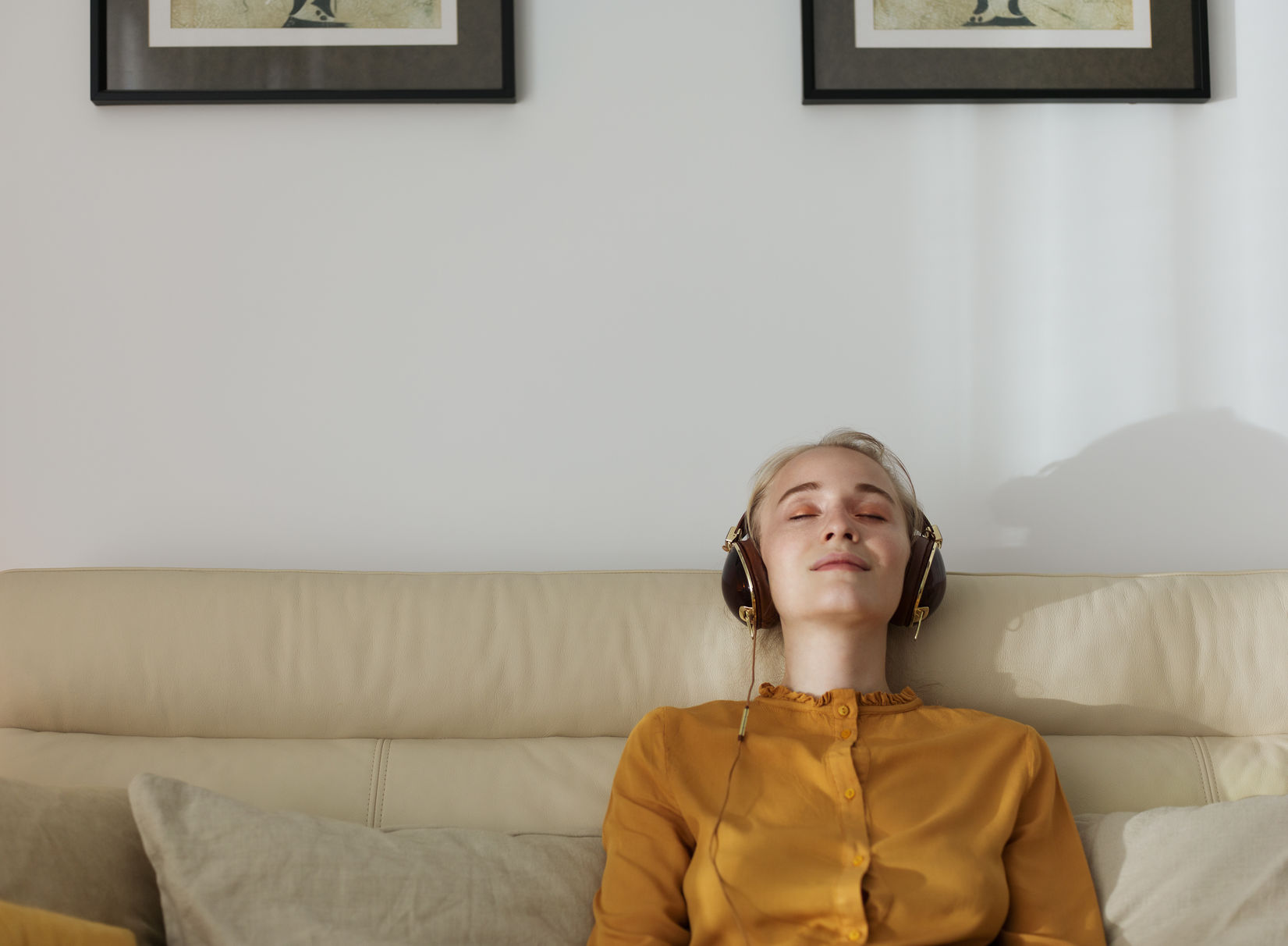 Young casual woman sitting on couch listening to music with earphones keeping eyes closed.
