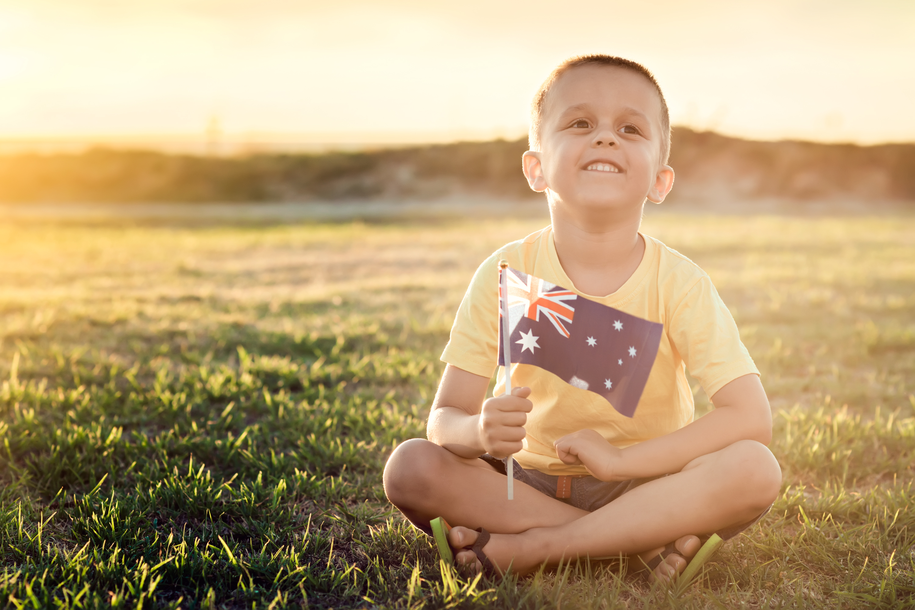 Boy with Australian Flag sitting on the grass on Australia Day at sunset