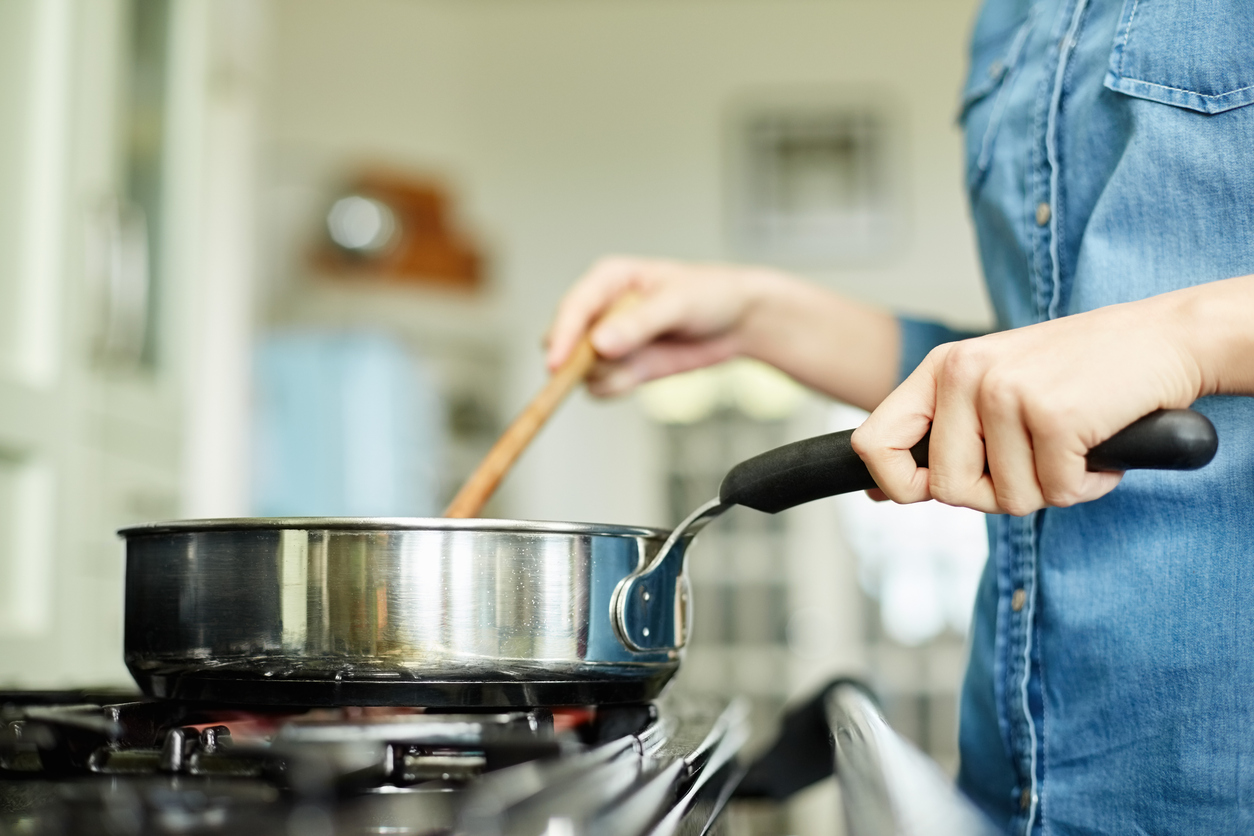 Midsection below view image of woman cooking food in pan. Utensil is placed on gas stove. Female is stirring dish in frying pan. She is preparing food in domestic kitchen.